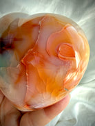 Close- up angle of a polished Carnelian heart showing flowing orange and golden mineral patterns in natural light