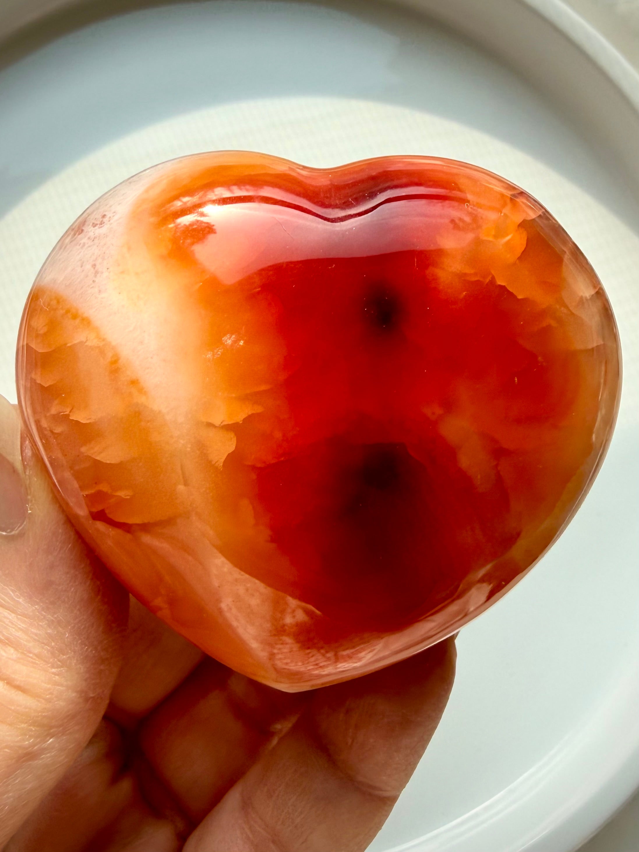 Hand holding Carnelian heart with molten orange banding and creamy white swirls, Sacral Chakra crystal for vitality and courage