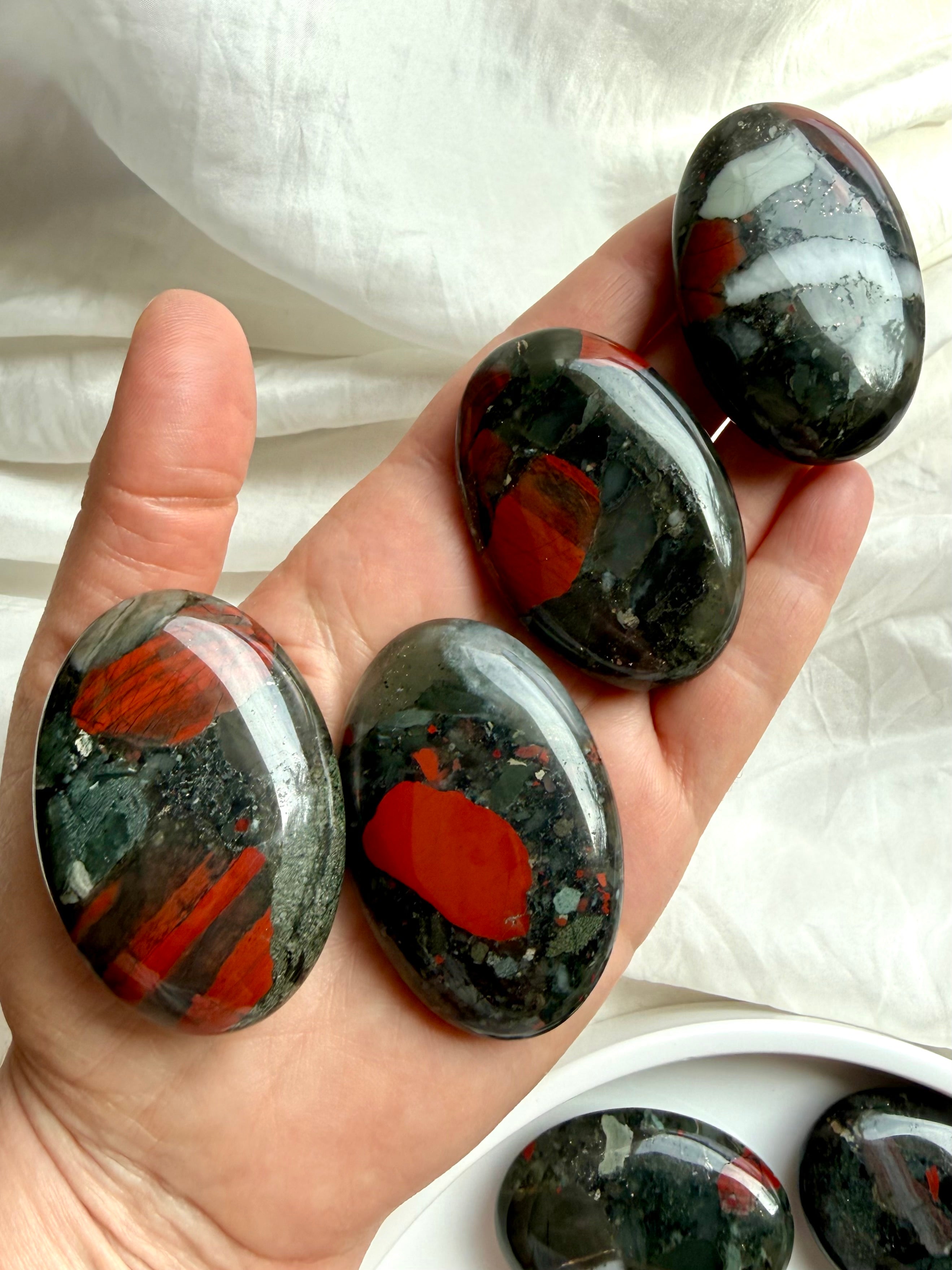 Bloodstone palm stones held in hand showing unique red, green and dark mineral patterns for grounding and vitality