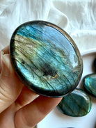 Blue and teal flash Labradorite palm stone held in hand with polished natural crystal finish