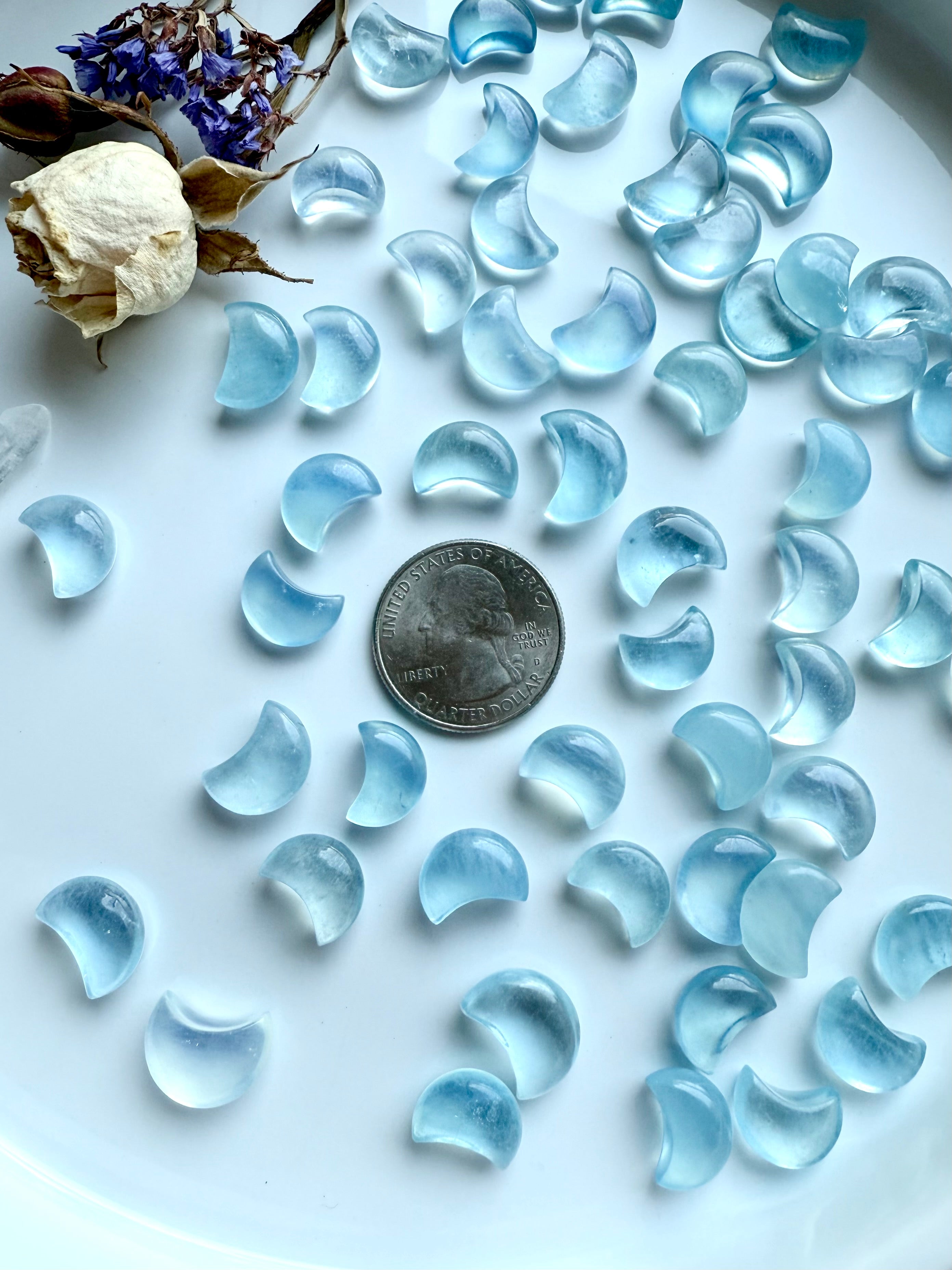 Aquamarine crystal moons surrounding a US quarter for size reference — tiny crescent carvings for crystal grids and moon rituals