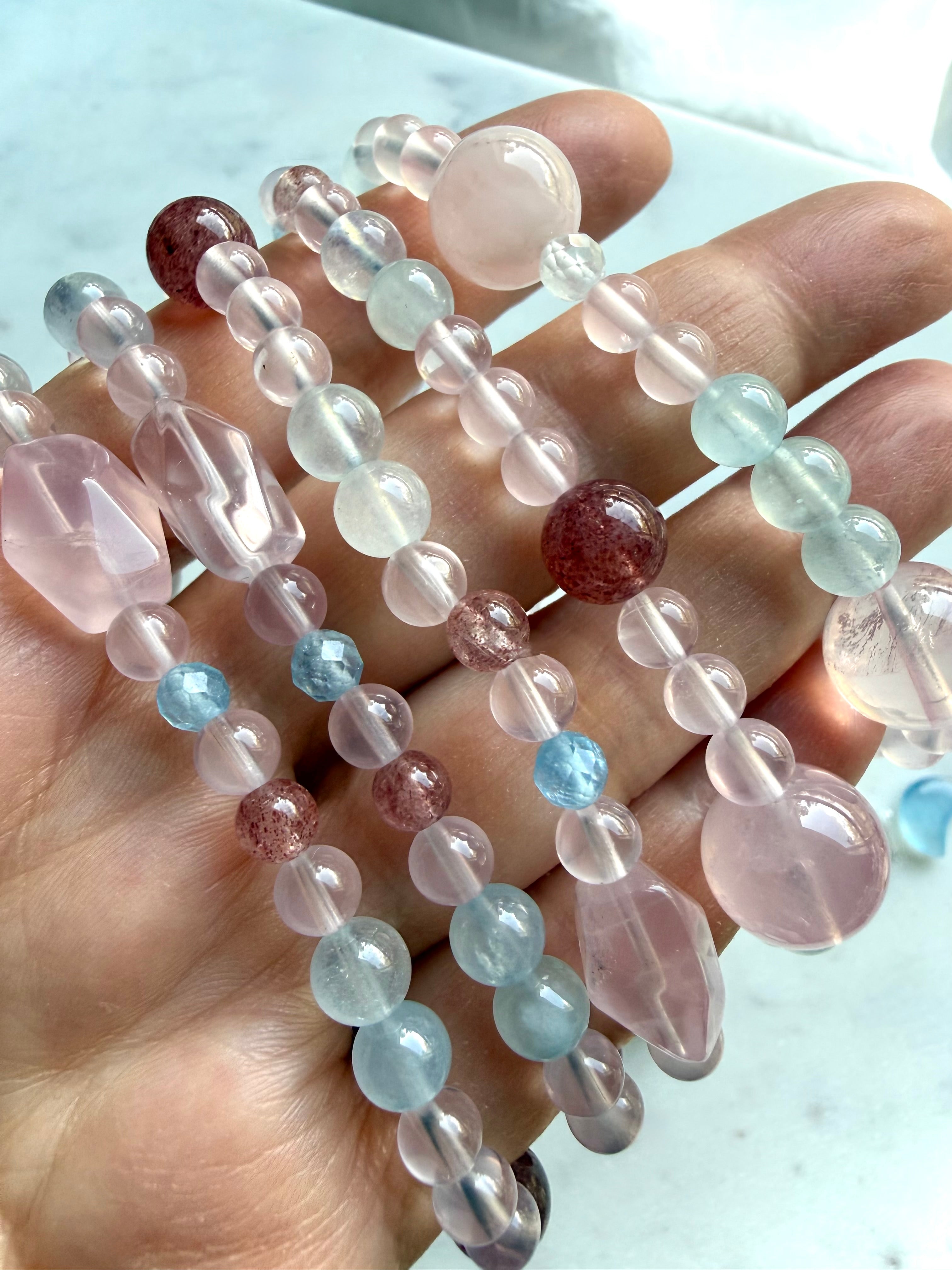mixed bead crystal bracelets draped across hand showing multiple sizes and shapes, rose quartz aquamarine strawberry quartz jewelry with soft pink and blue tones