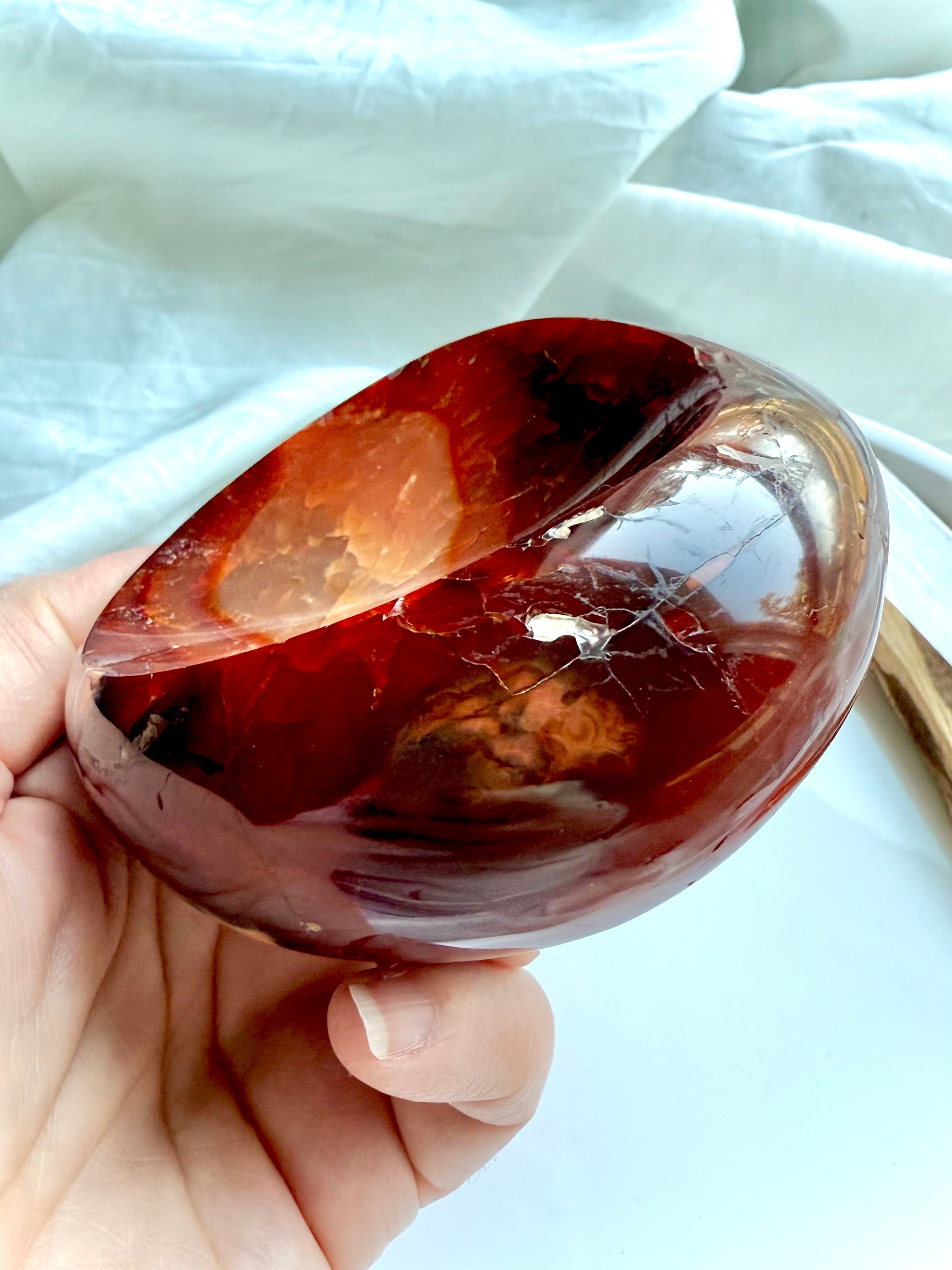 Hand holding polished Carnelian crystal bowl with fiery orange-red tones and natural inclusions – carved gemstone dish for altar or jewelry