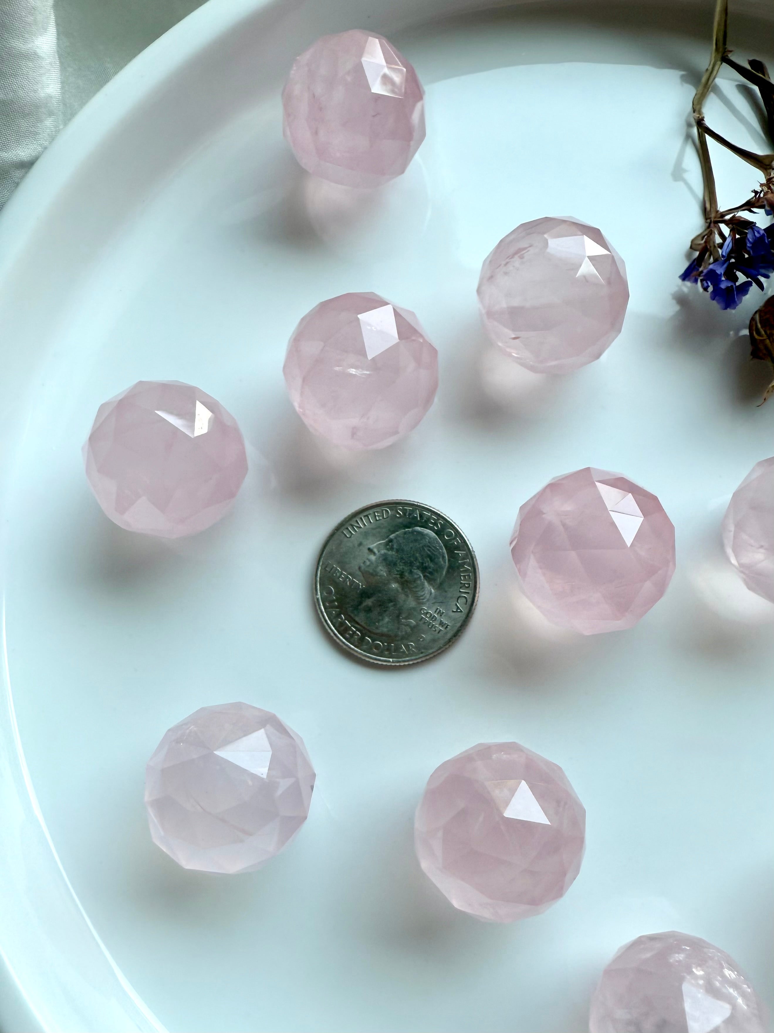Faceted pink crystal balls on a white plate with a US quarter for scale.