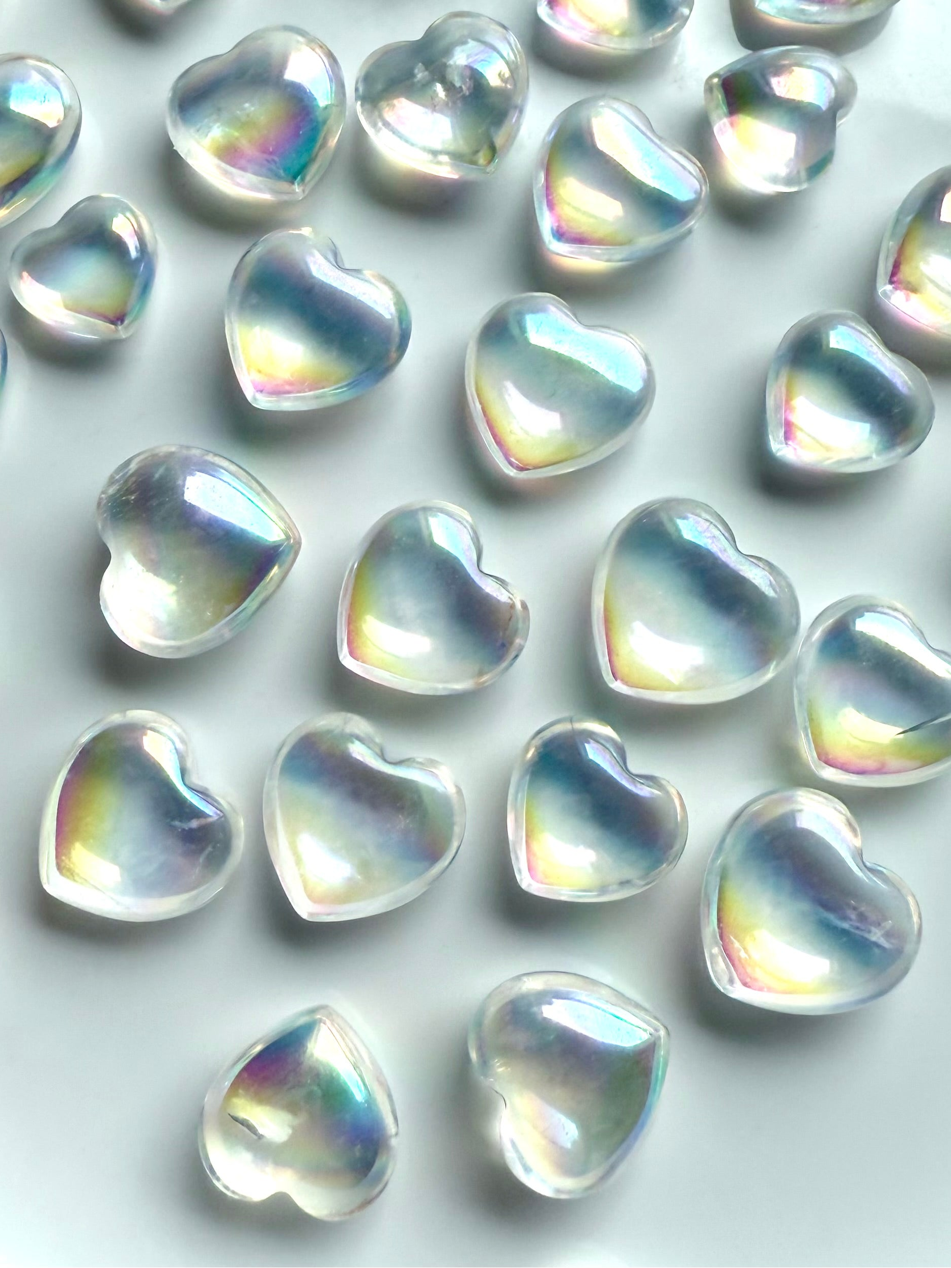 Closeup of rainbow aura quartz hearts shining with opalescent glow on a white dish