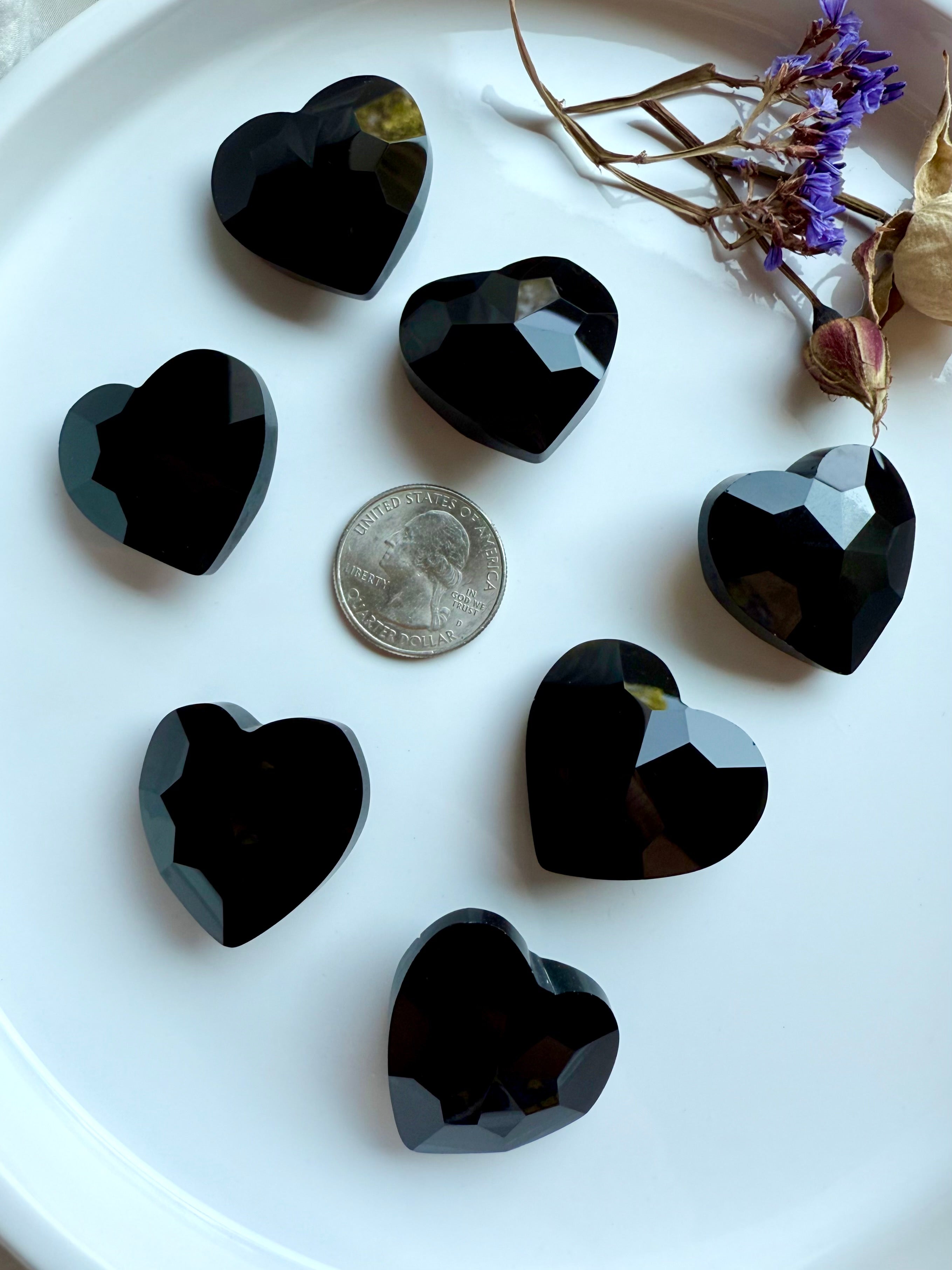 Faceted obsidian heart stones on a white surface with a US quarter for scale.