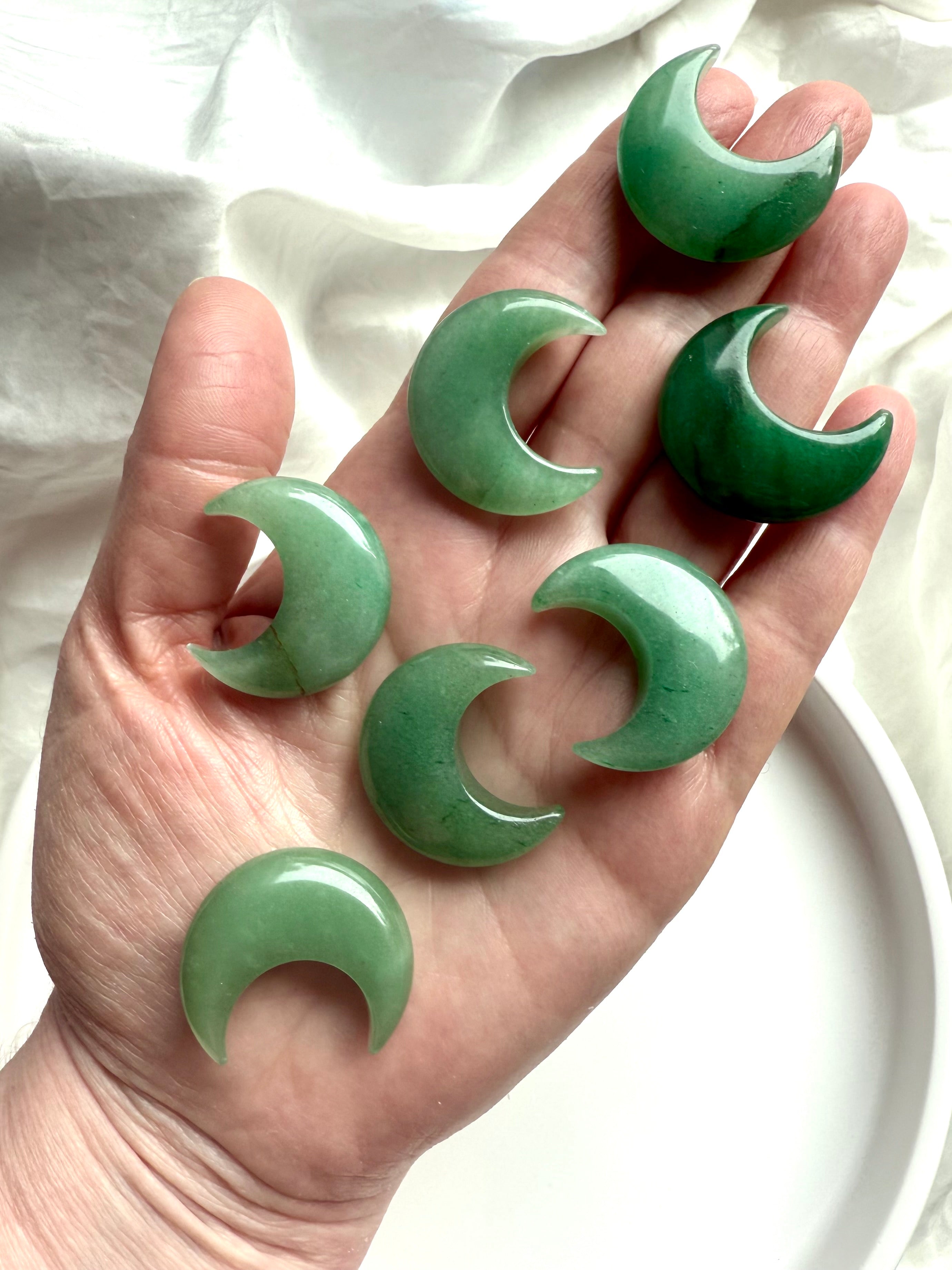 Green Aventurine crescent moons displayed on hand over white silk, Heart Chakra crystals for healing, peace, and grounding