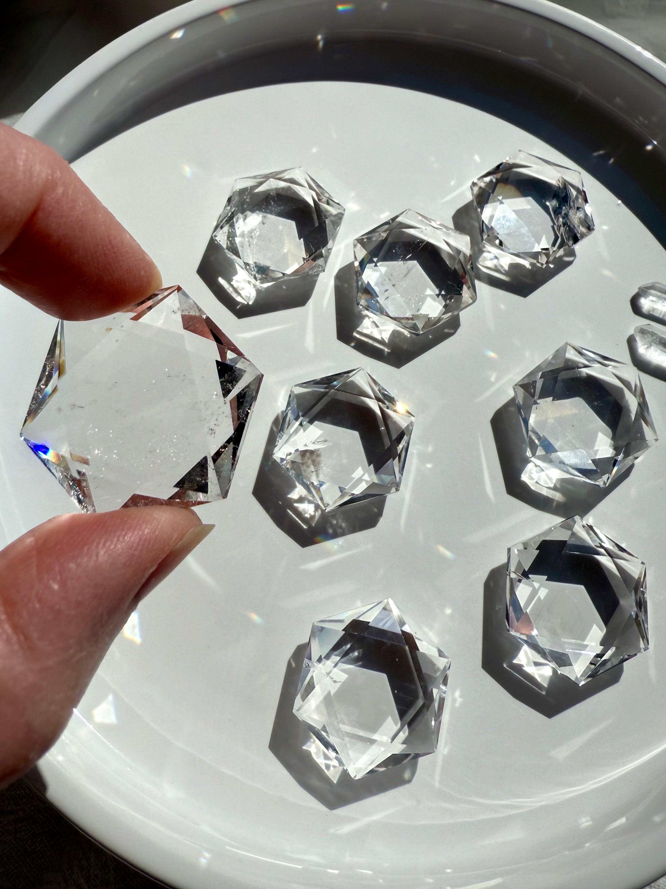 Overhead of plate full of Clear Quartz hexagons in bright sunlight, reflective facets sparkling with one held in foreground