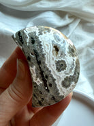 Polished Ocean Jasper crescent moon in neutral gray tones with bold starburst orbs, calming stone for strength and stability
