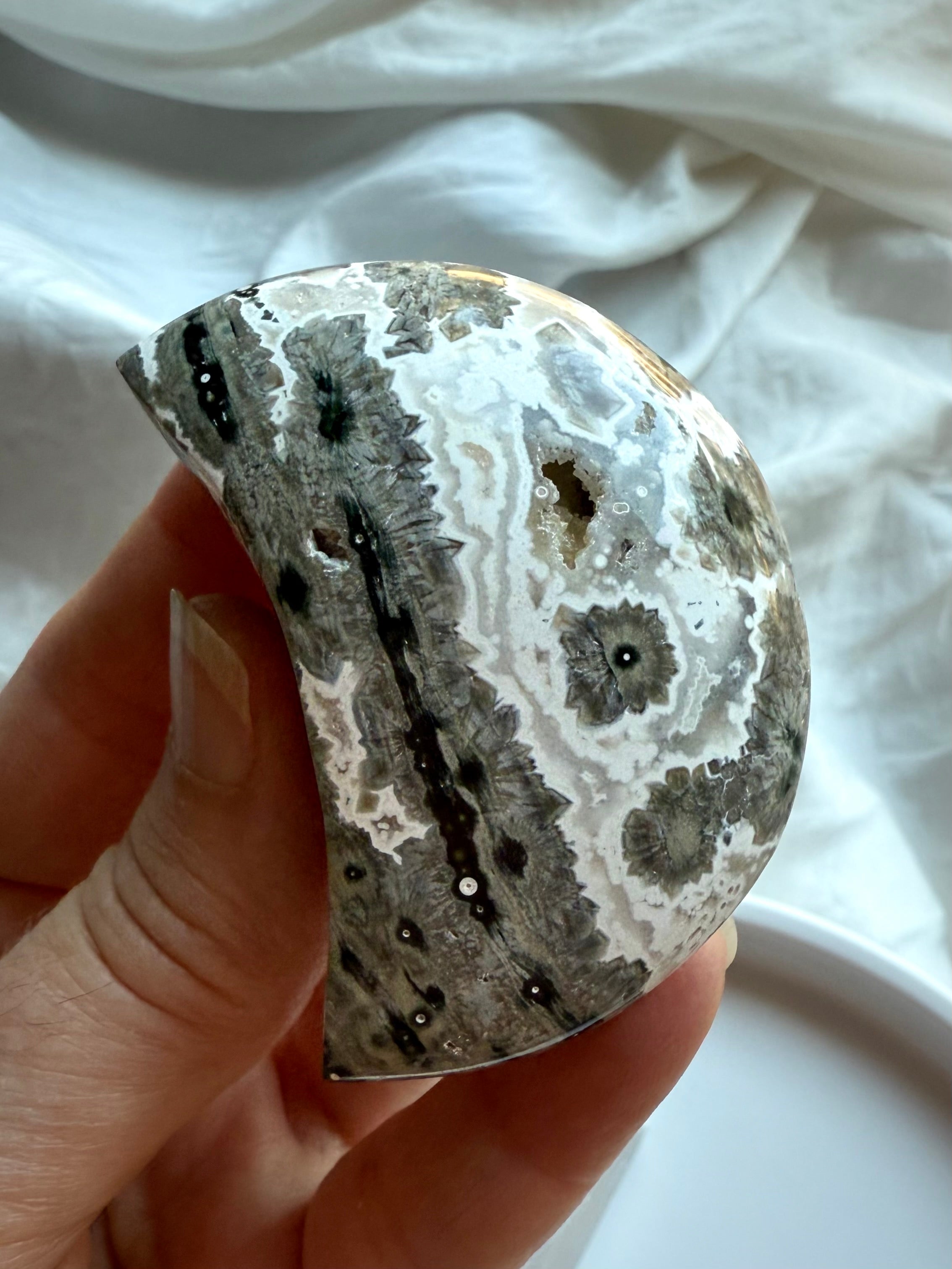 Polished Ocean Jasper crescent moon in neutral gray tones with bold starburst orbs, calming stone for strength and stability
