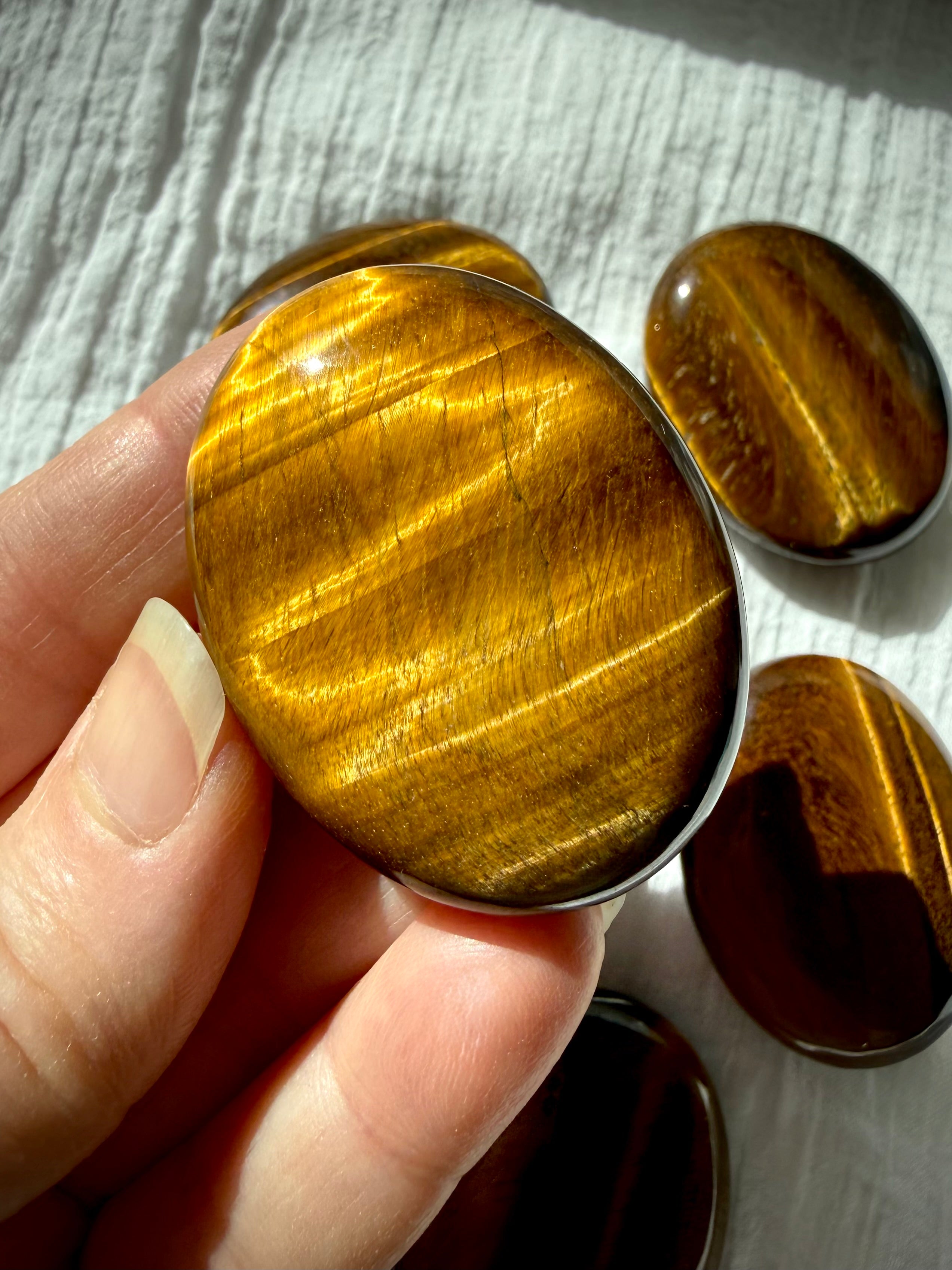 Closeup of a polished Tiger’s Eye palm stone with vibrant golden chatoyancy and deep brown banding