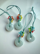 Four jade donut keychains with rainbow lucky knots laid on a glossy white dish