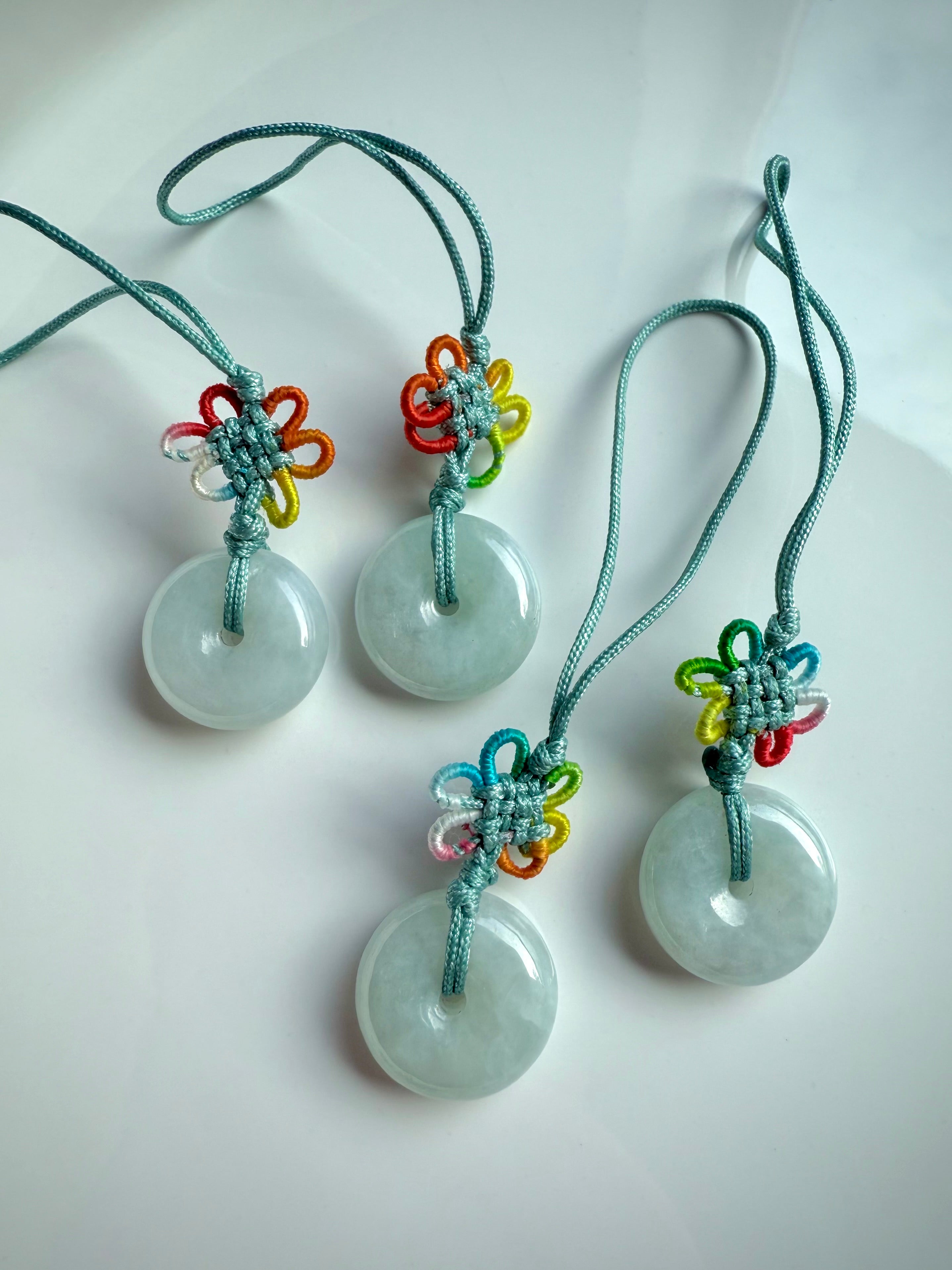 Four jade donut keychains with rainbow lucky knots laid on a glossy white dish