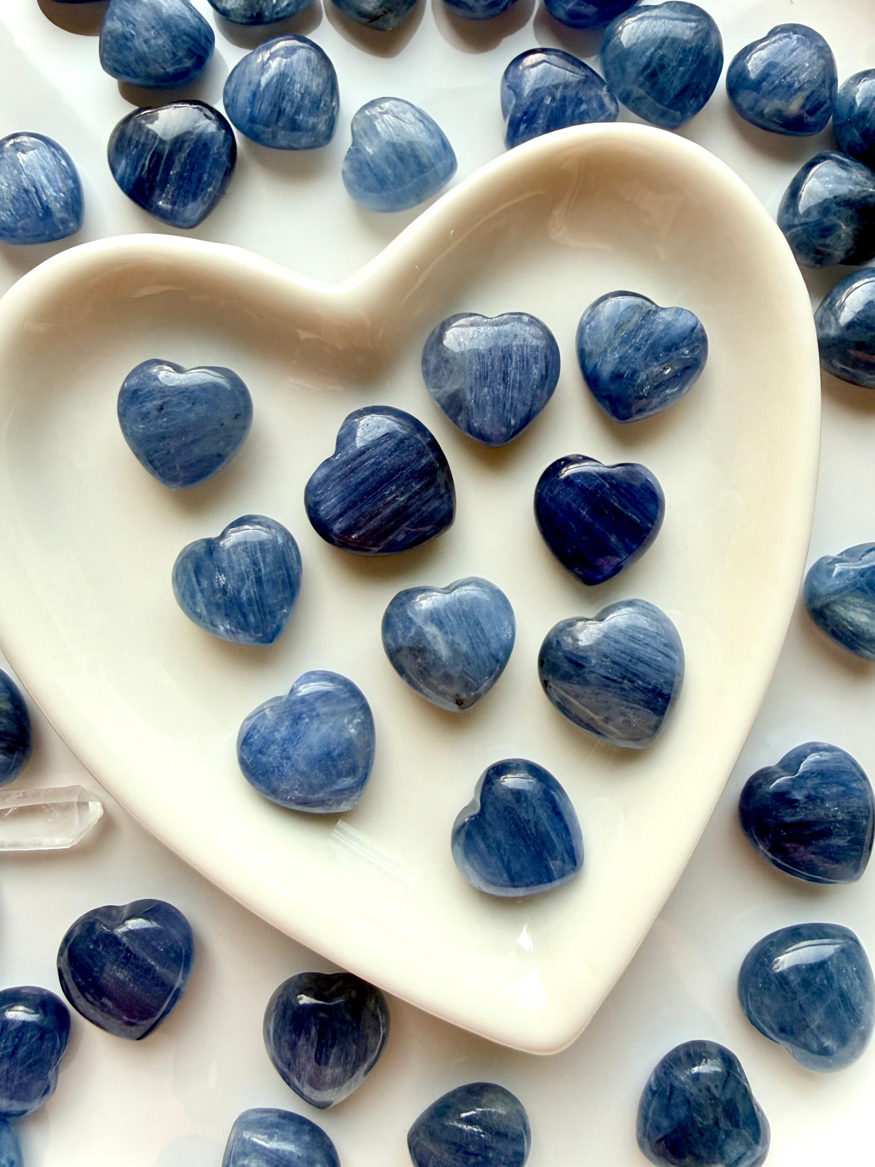 Mini Blue Kyanite heart crystals displayed in a white heart bowl with additional hearts in the background, throat chakra stones for communication and calm