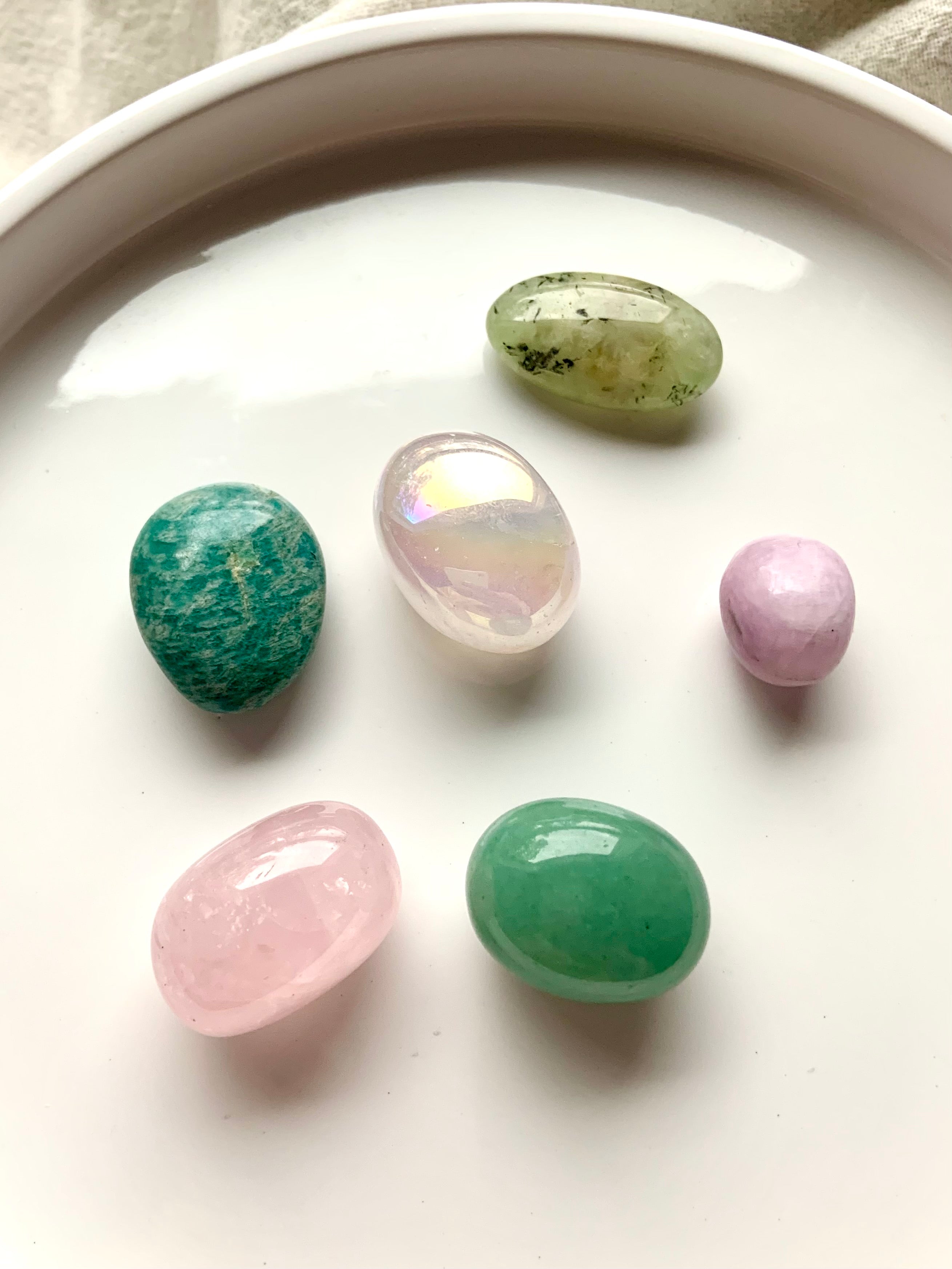 Heart Chakra healing stones set of 7 crystals arranged on a white plate — includes aura rose quartz, rose quartz, kunzite, amazonite, prehnite, and green aventurine.