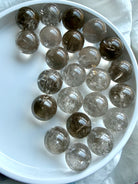 Small polished Smoky Quartz spheres arranged in white bowl with grounding crystal energy aesthetic