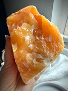 Handheld Orange Calcite mineral specimen showing natural texture, translucency, and layered formations