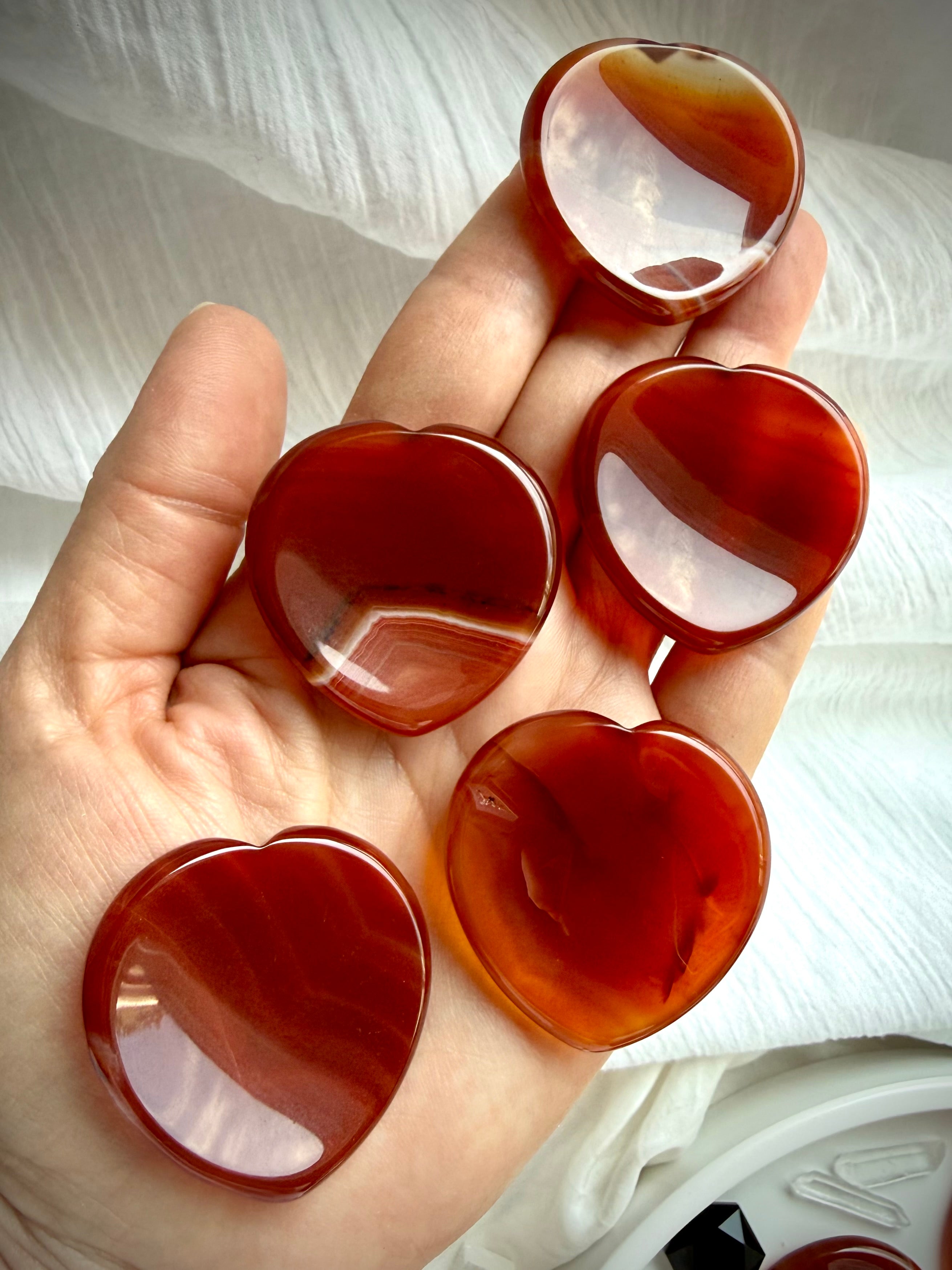 Carnelian heart worry stones held in hand showing glossy polish, rich red-orange color and natural translucent variation