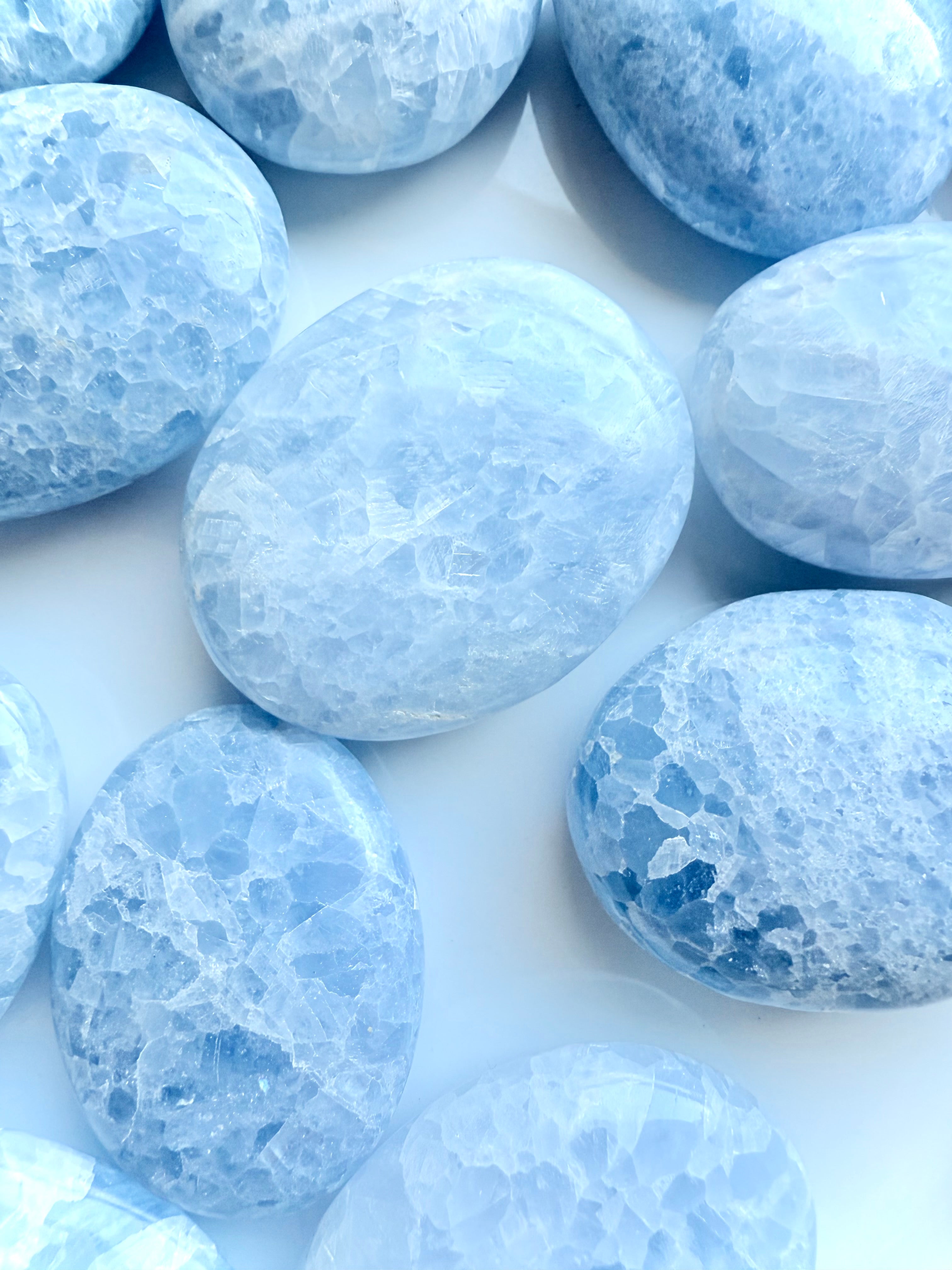 Grouping of polished Blue Calcite palm stones on white surface — gentle healing crystals for Throat Chakra and stress relief