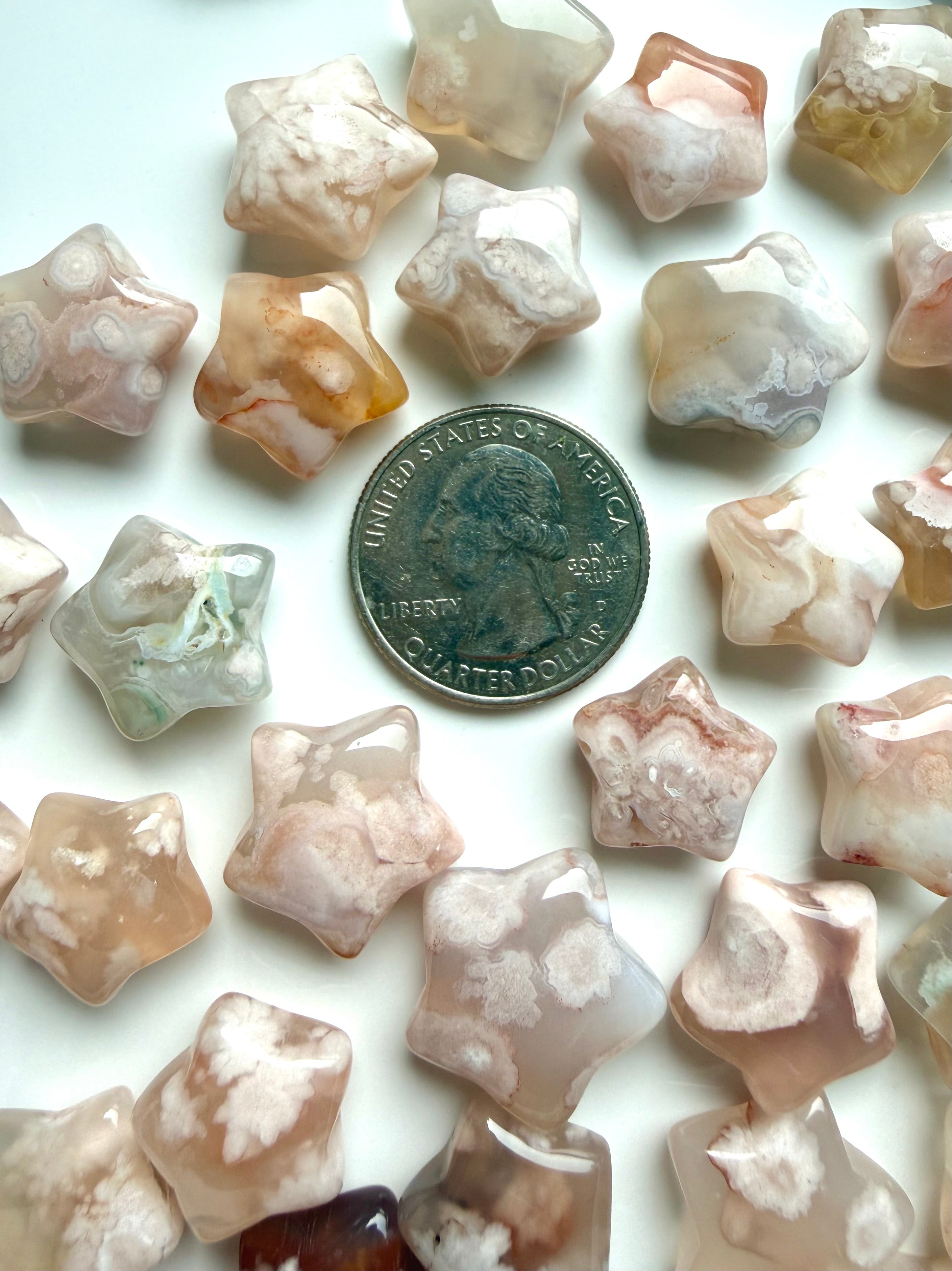 Flower Agate star carvings shown with a US quarter for scale, with creamy pink, peach, and taupe natural inclusions