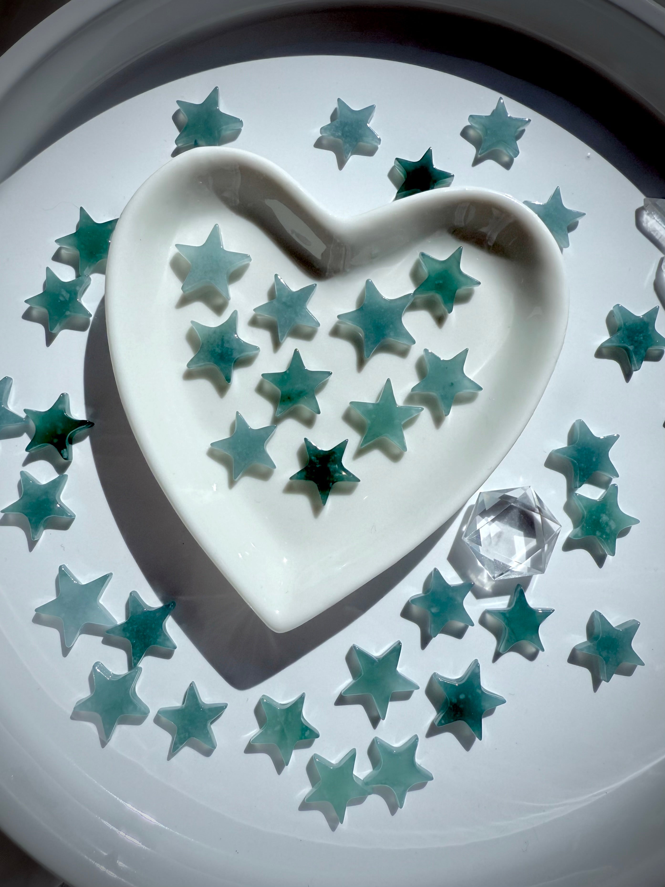 Our Mini Blue Water Jade Stars shown on a white plate photographed in bright direct sunlight