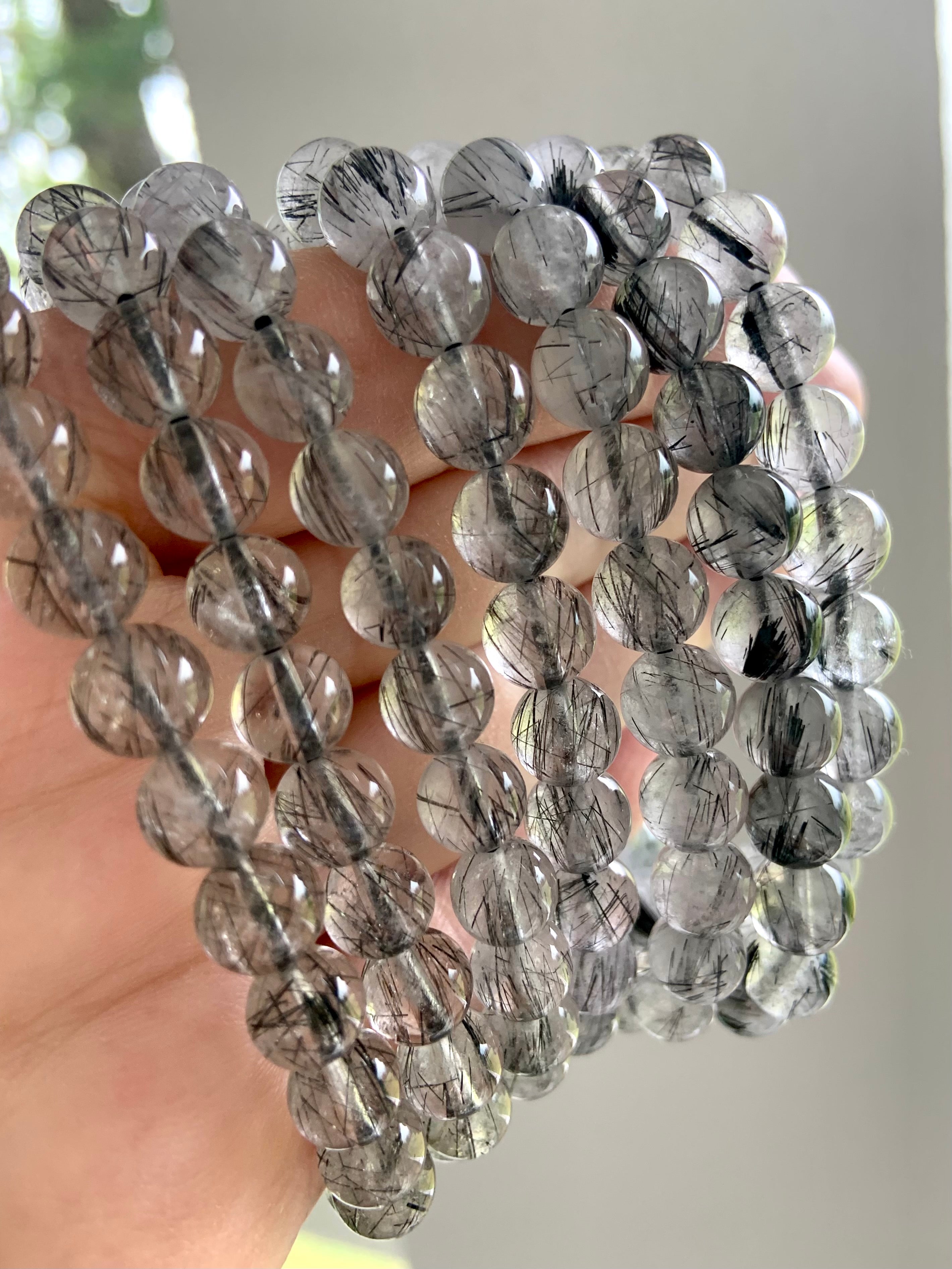 Closeup of Black Tourmaline in Quartz bracelets held to the light, revealing clarity and suspended needle-like inclusions