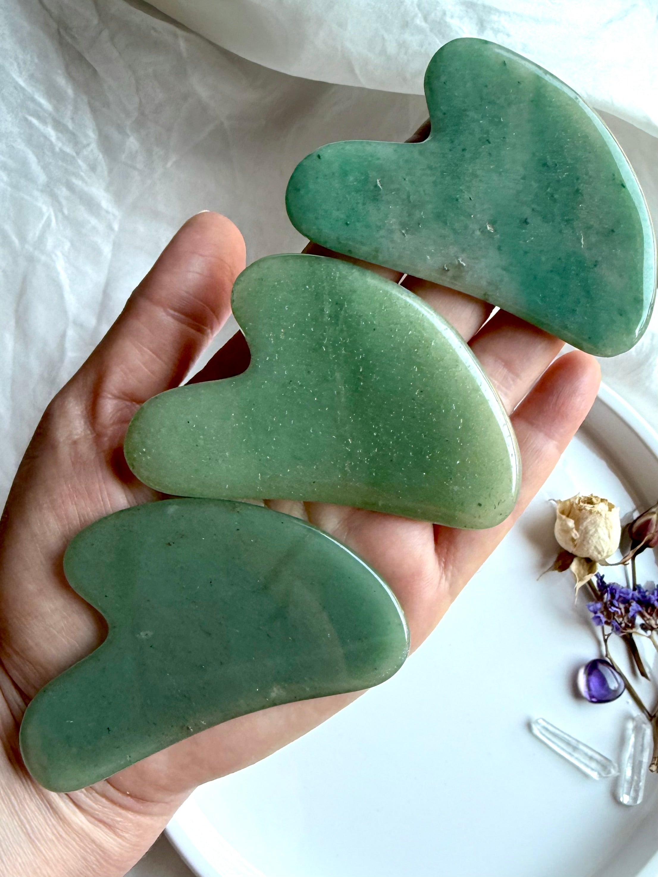 Hand holding three Green Aventurine crystal gua sha facial massage tools with smooth curved contour design