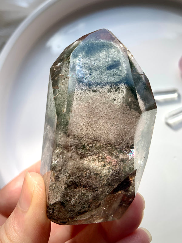 Four Seasons Garden Quartz Tower with Rainbows and chlorite phantoms held in my fingertips on a light colored background