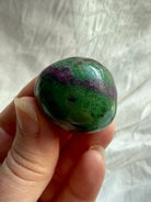 Ruby Zoisite tumbled crystal held between fingers, displaying deep green Zoisite, natural ruby inclusions and glossy polished finish