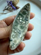 Orbicular Ocean Jasper crescent moon with gray, olive, and cream bullseye patterns, side view