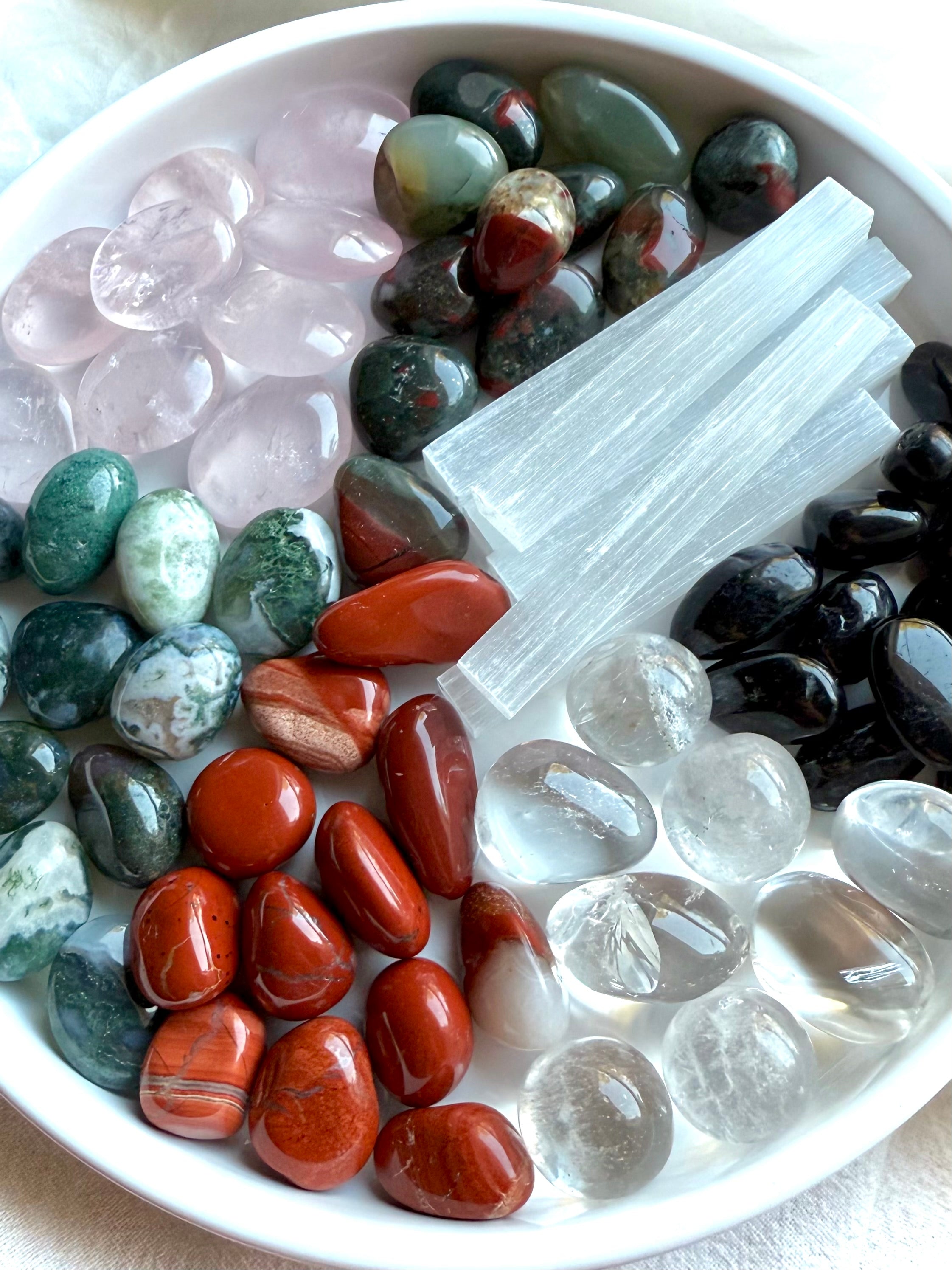 Variety of Bloodstone, Rose Quartz, Red Jasper, and more healing crystals on a white plate