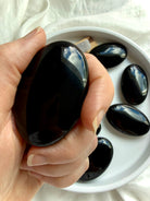 Black Obsidian palm stone cradled in hand for grounding, emotional resilience, and energetic protection