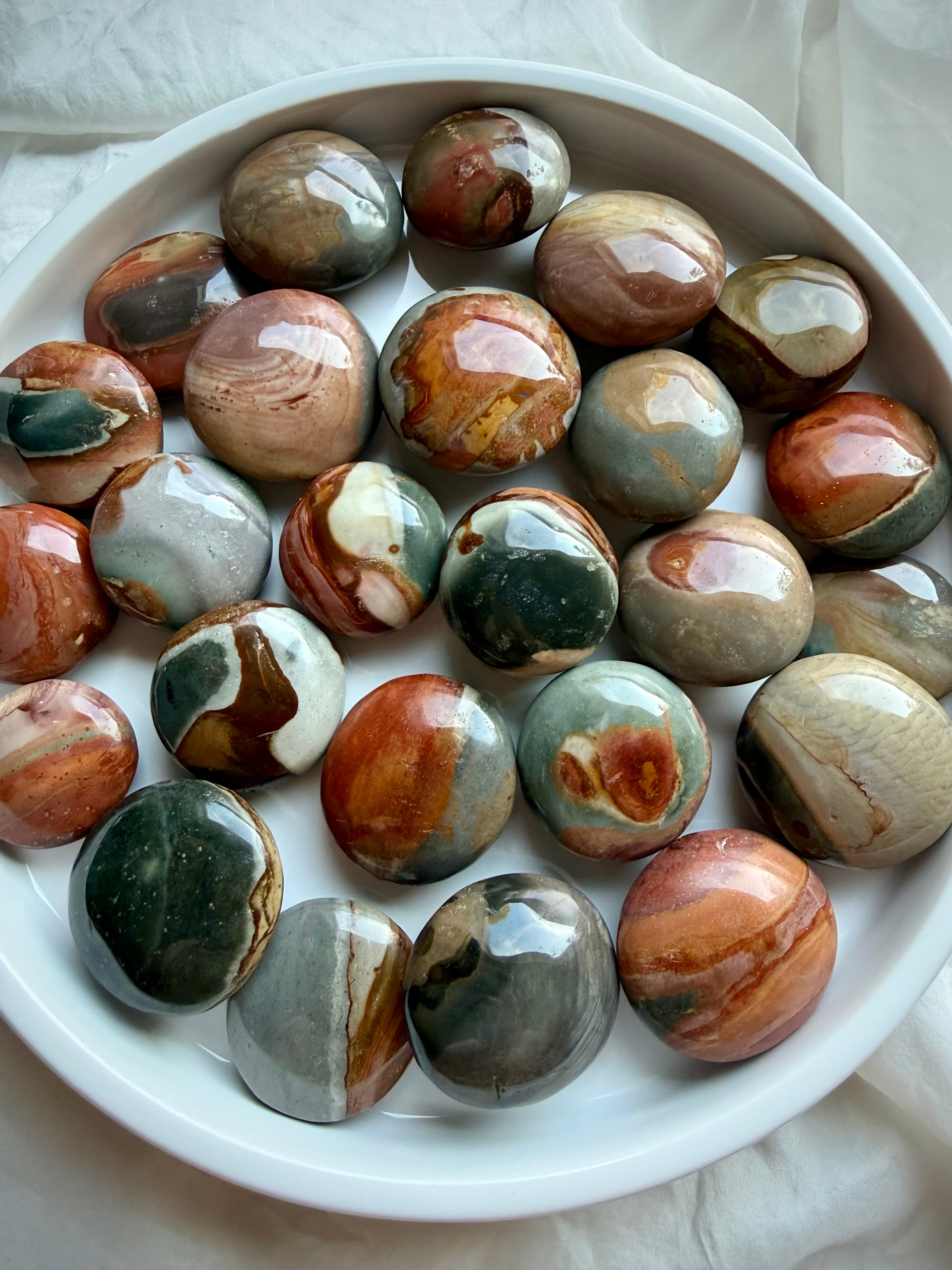 Mini Polychrome Jasper palm stones from Madagascar in a white bowl, showcasing earthy red, green, cream, gray, and brown landscape patterns