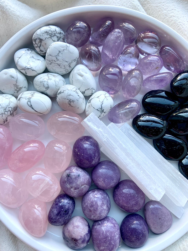 A close up view of the crystals inside the Sweet Sleep Crystal Set, made to help you relax at bedtime. Set contains 6 crystals: lepidolite, amethyst, rose quartz, howlite, black tourmaline + selenite. Comes in a carrying pouch with an info card to help you ID the crystals + start working with them.