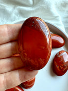 Closeup of oval Red Jasper palm stone — Root Chakra healing crystal for grounding and resilience.