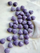 Collection of polished Lilac Lepidolite puffy hearts arranged on a marble background