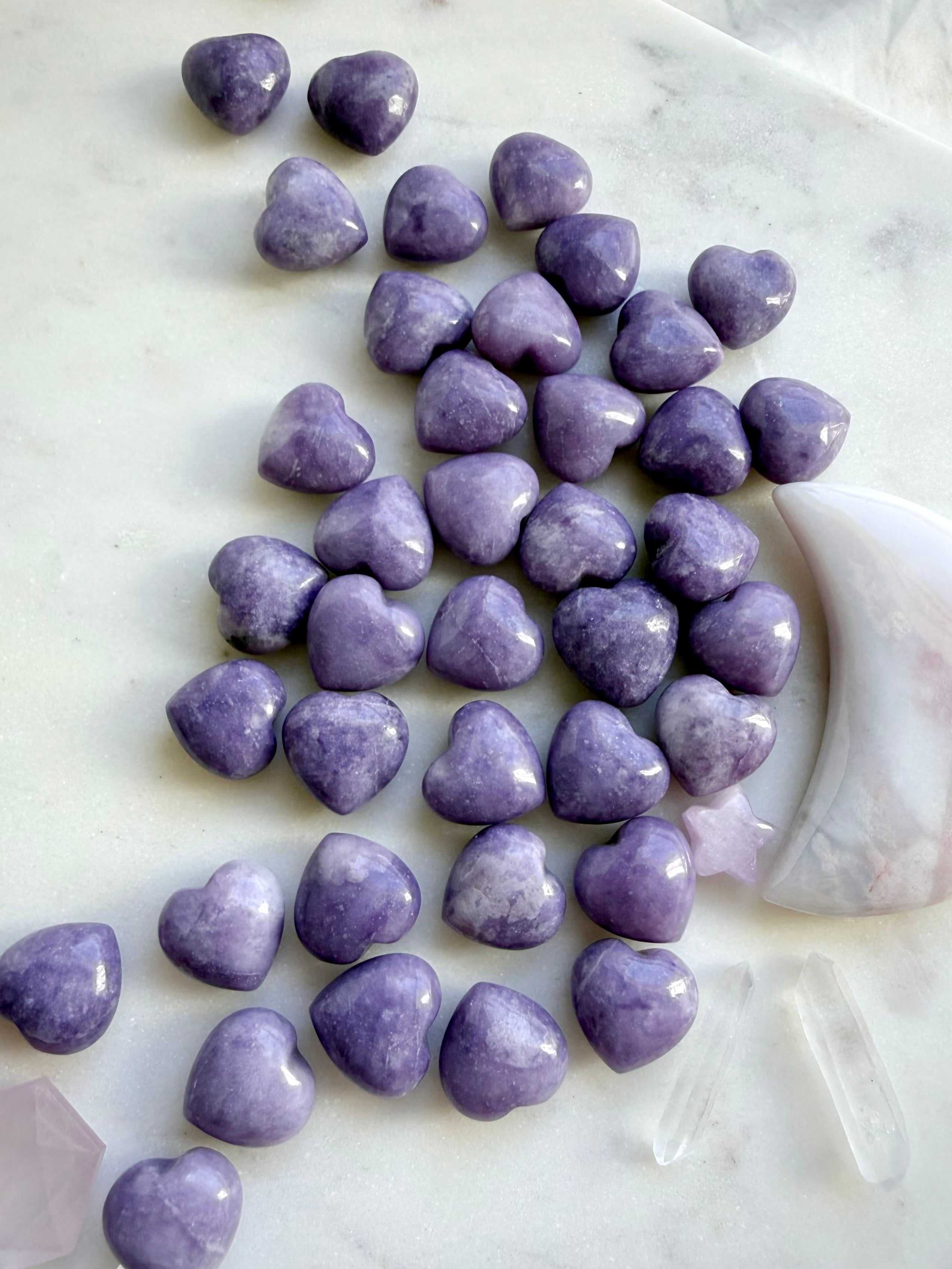 Collection of polished Lilac Lepidolite puffy hearts arranged on a marble background