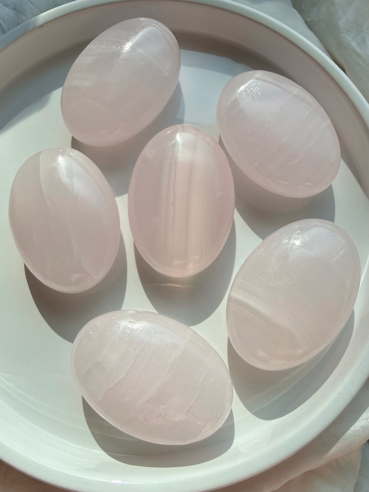 Polished Mangano Calcite palm stones displaying soft blush pink color and natural white banding