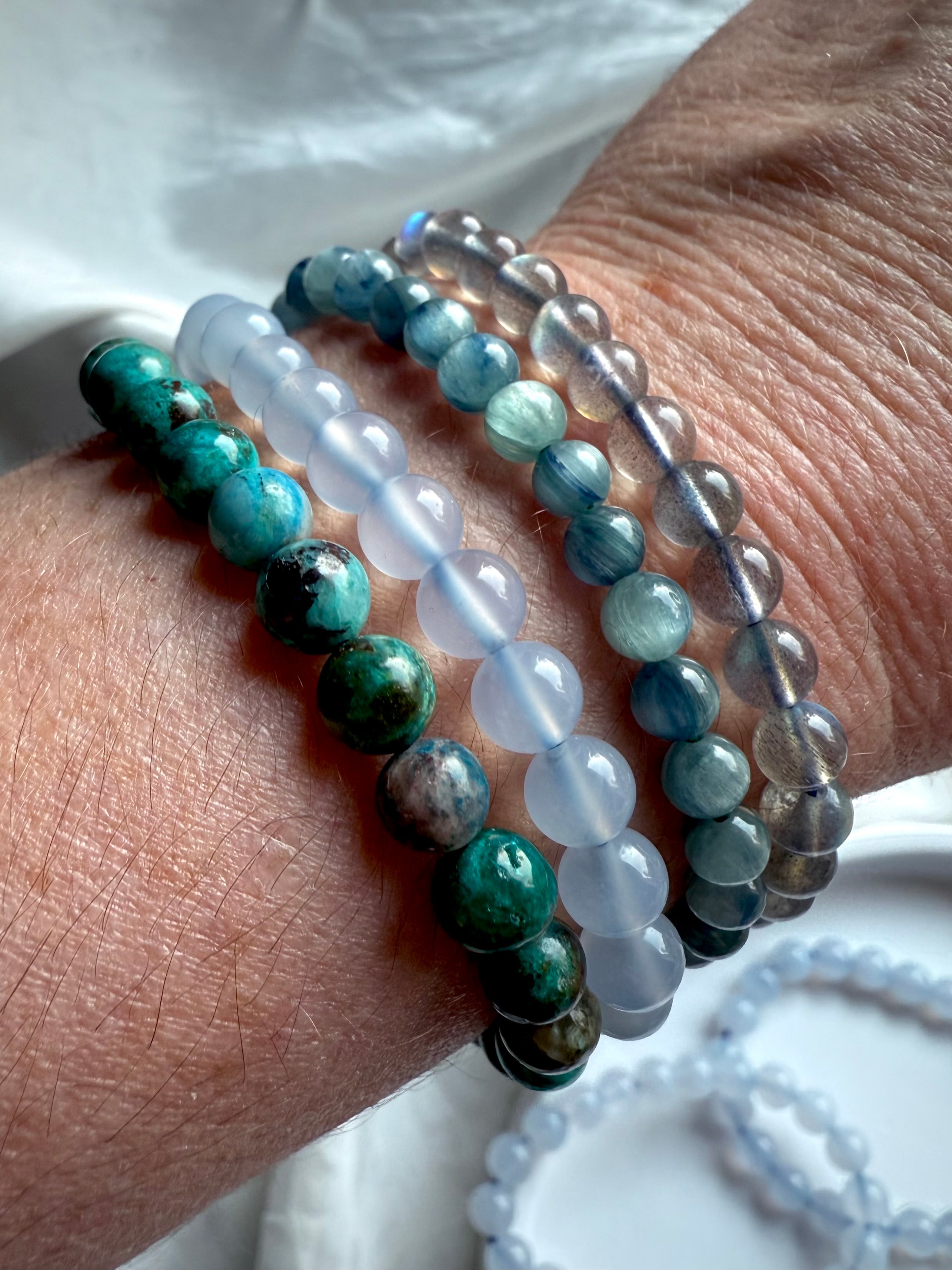 Stacked crystal bracelets on wrist including Blue Chalcedony, Chrysocolla, Aquamarine, and Labradorite — gemstone stack for serenity and balance.