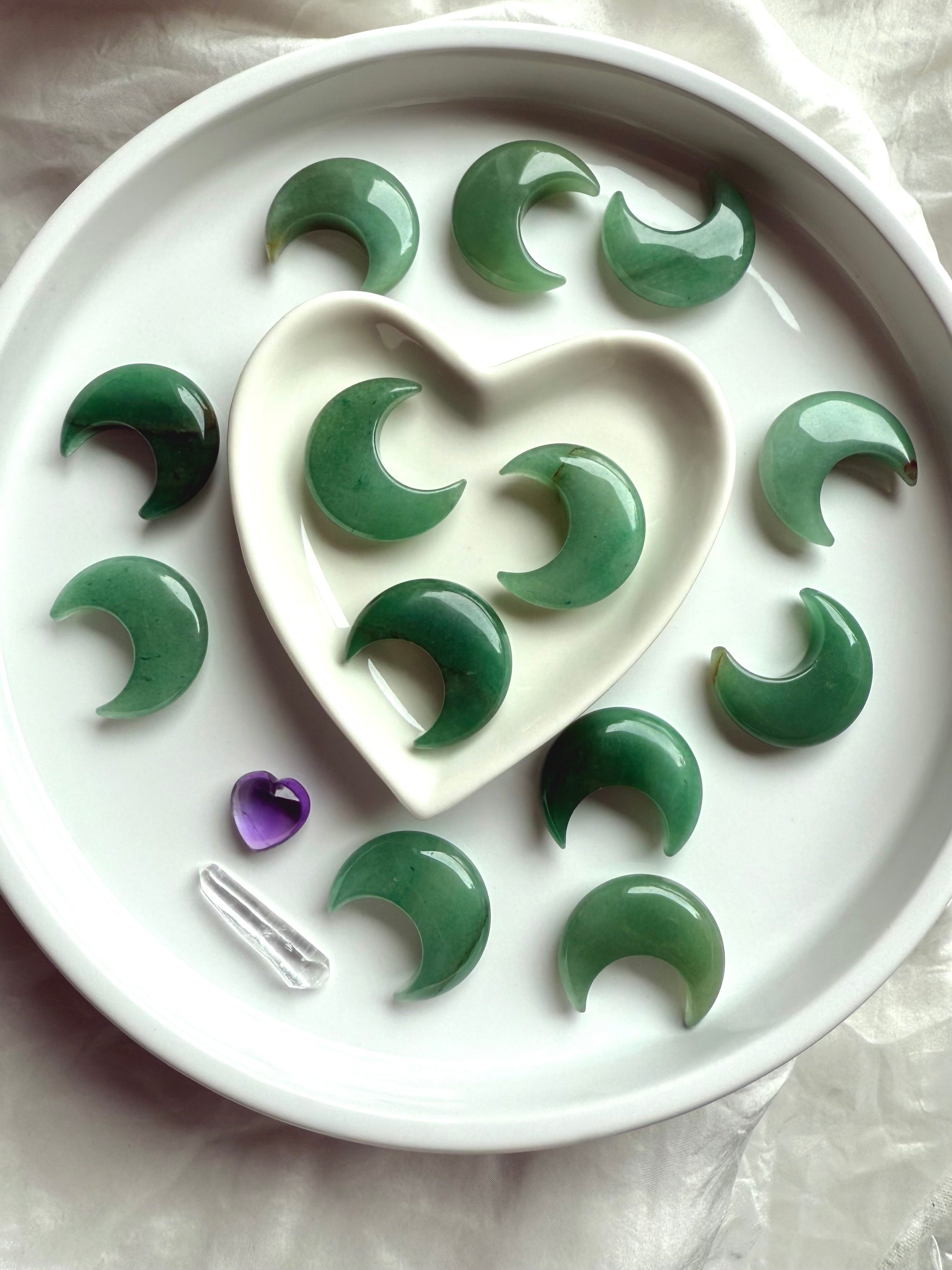 Wide view of Green Aventurine moons in a white heart bowl with additional moons surrounding, altar décor for Heart Chakra energy