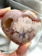 Hand holding a polished Pink Amethyst Flower Agate heart with druzy and soft white floral plume inclusions
