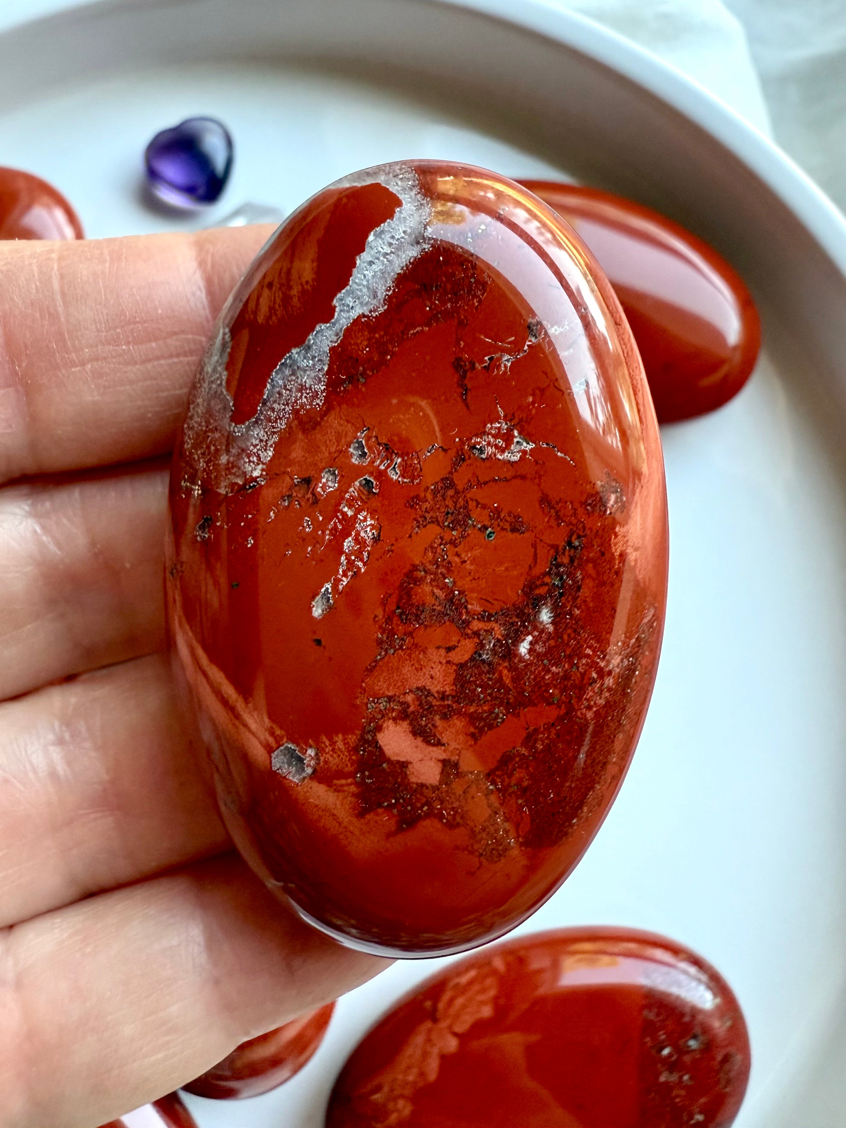 Close-up of polished Red Jasper palm stone — grounding crystal for Root Chakra healing and stability.