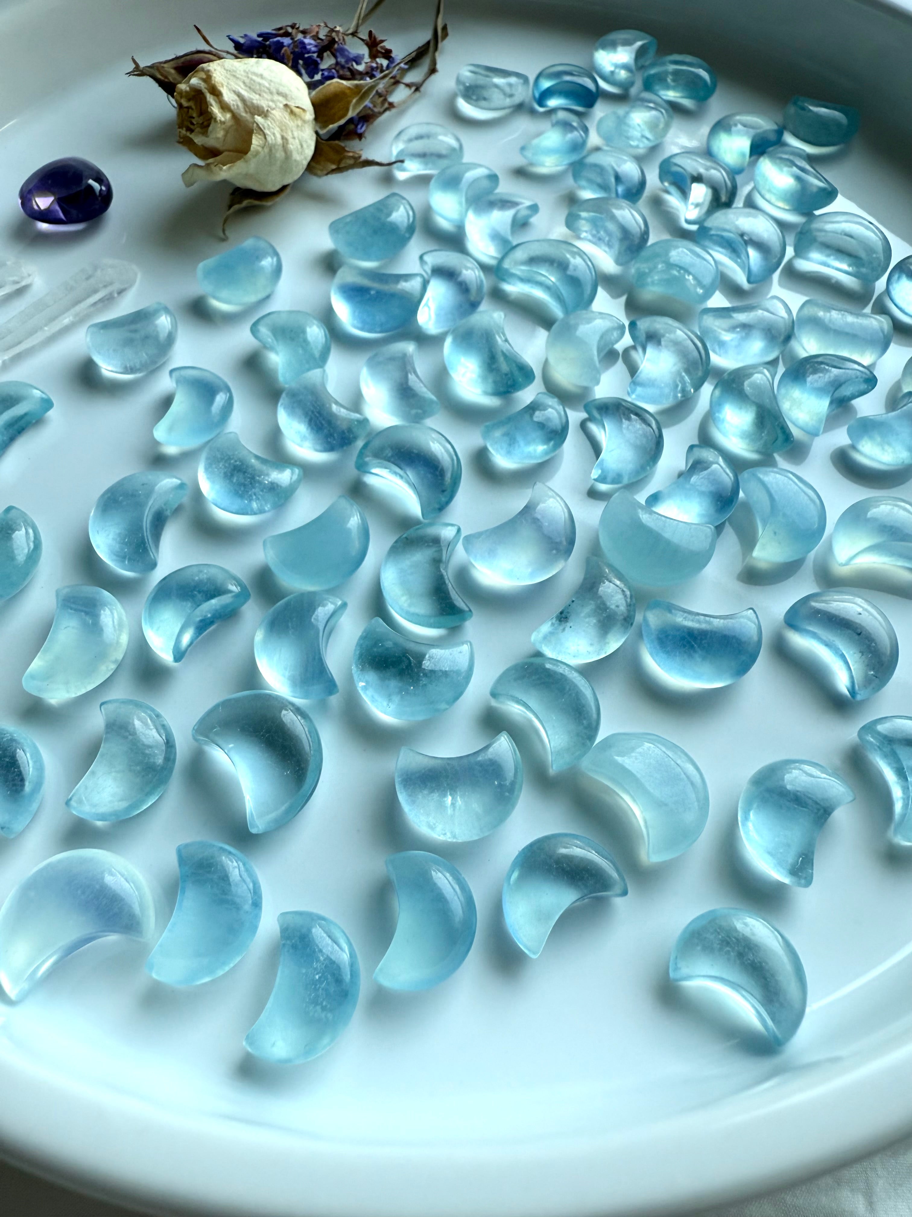 Angled side view of Aquamarine Mini Moons on a white tray with dried botanicals — gemstone moon carvings with soft translucent energy