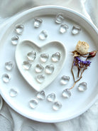 Mini Clear Quartz crystal hearts arranged in white heart bowl with additional hearts on tray with dried flowers