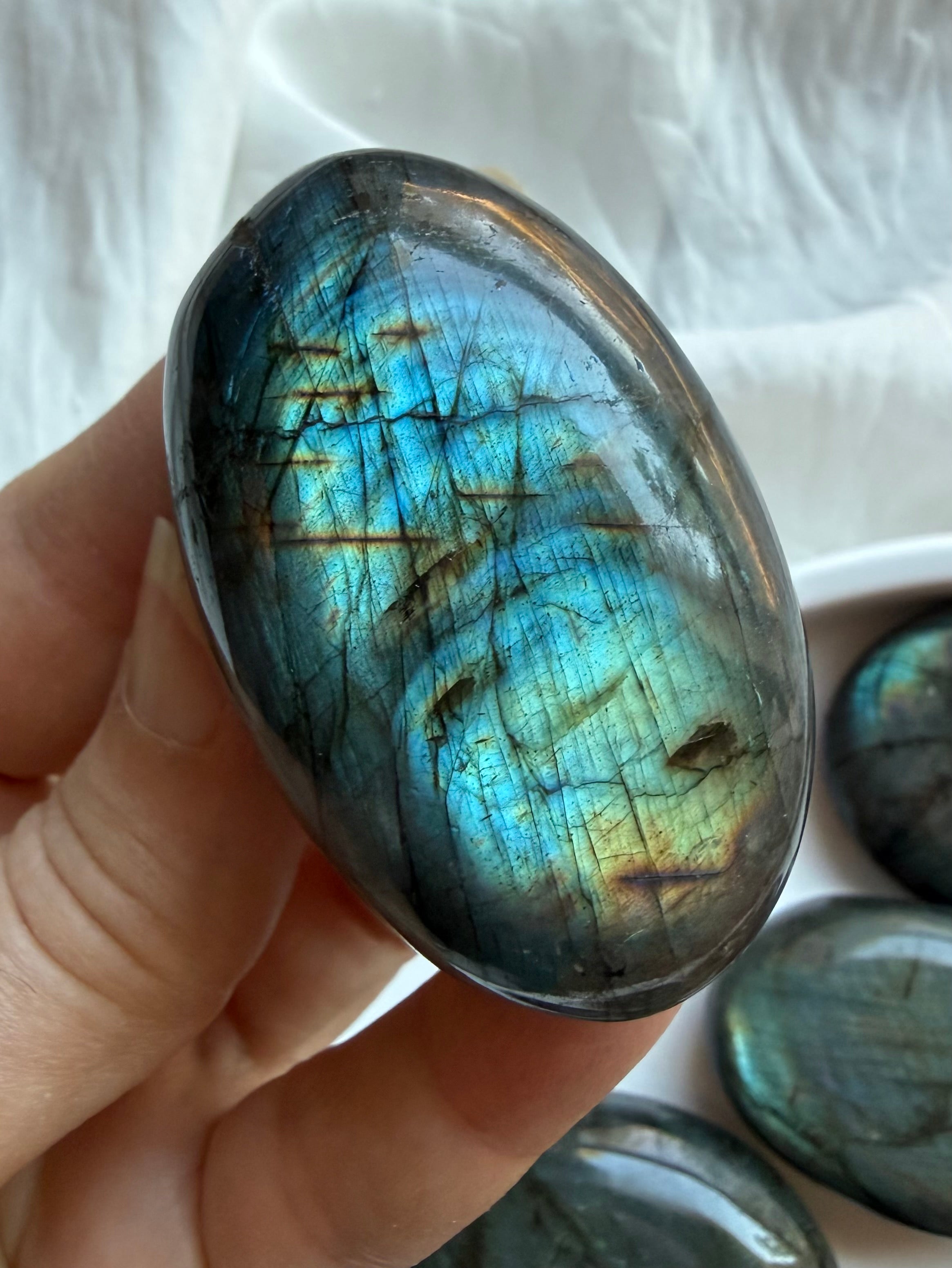 Labradorite palm stone held in hand with vivid teal green flash and natural mineral inclusions