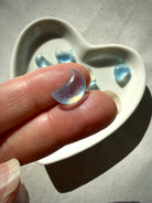 Closeup of a tiny Aquamarine crescent moon carvings resting on fingertips in natural lighting