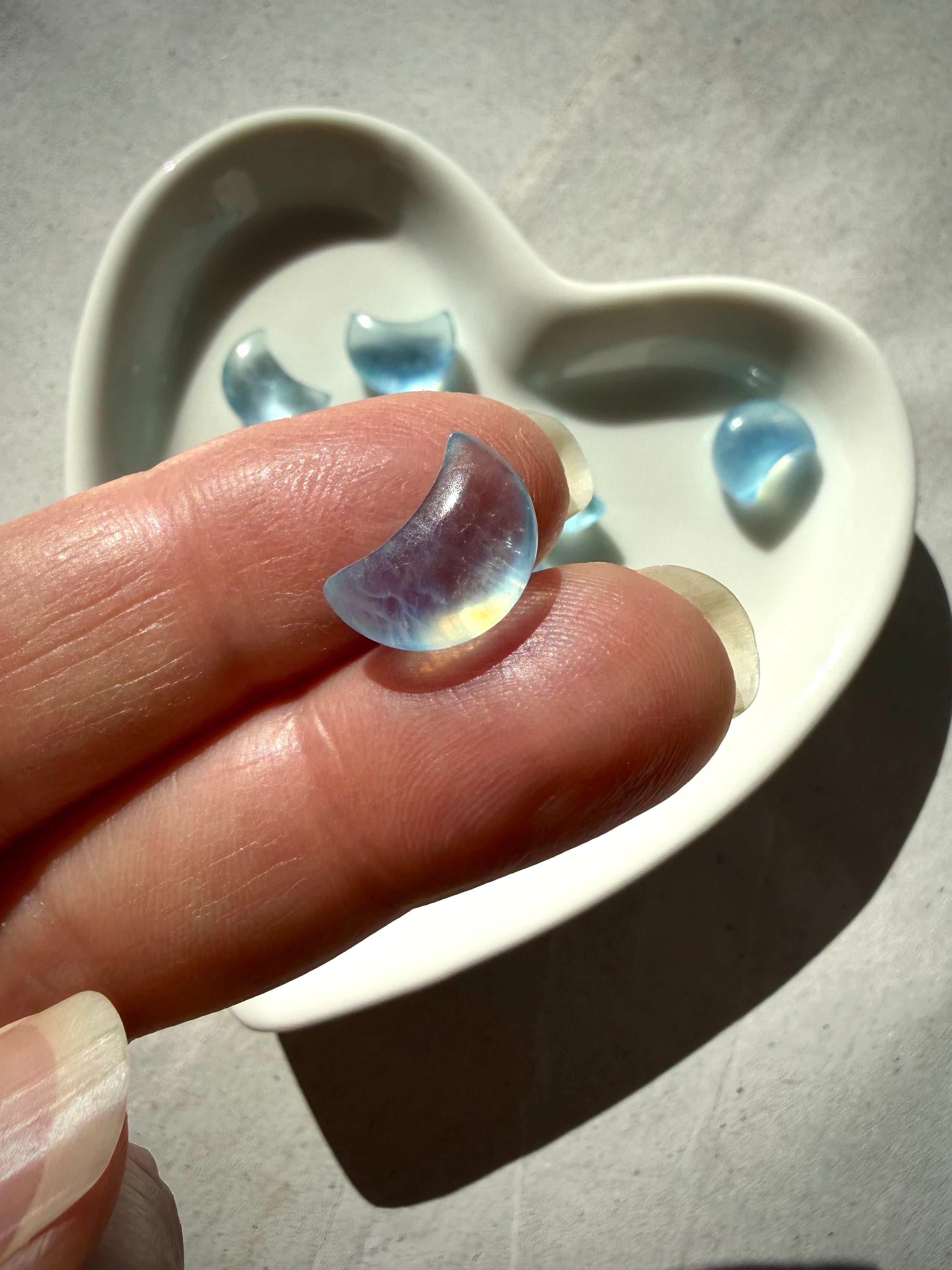 Closeup of a tiny Aquamarine crescent moon carvings resting on fingertips in natural lighting