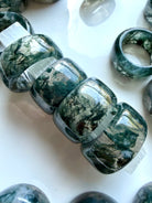 stacked moss agate wide band crystal rings showing natural landscape inclusions and earthy organic patterning