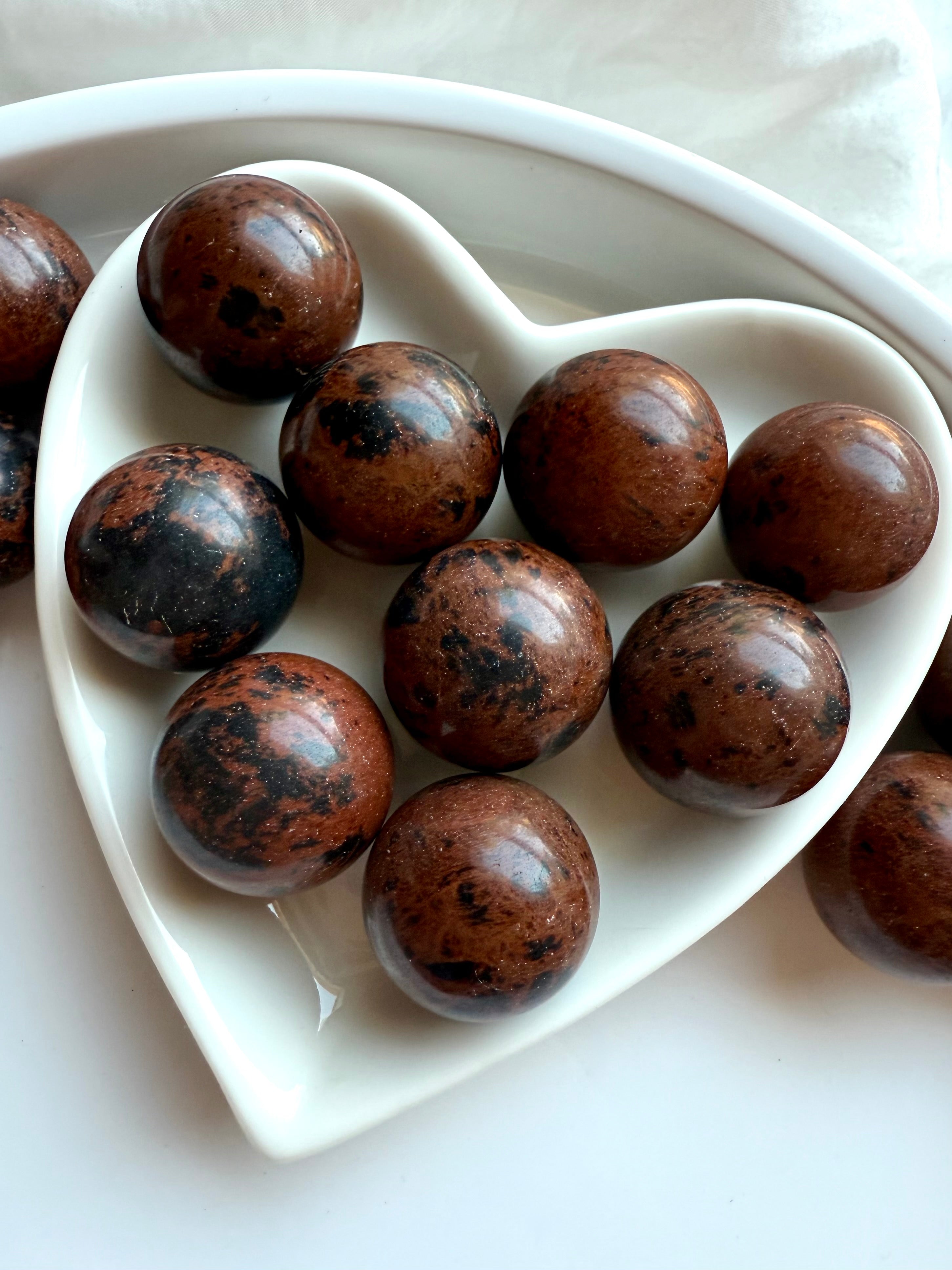 Close up of Mahogany Obsidian mini spheres arranged in white dish – protective healing crystals with natural inclusions