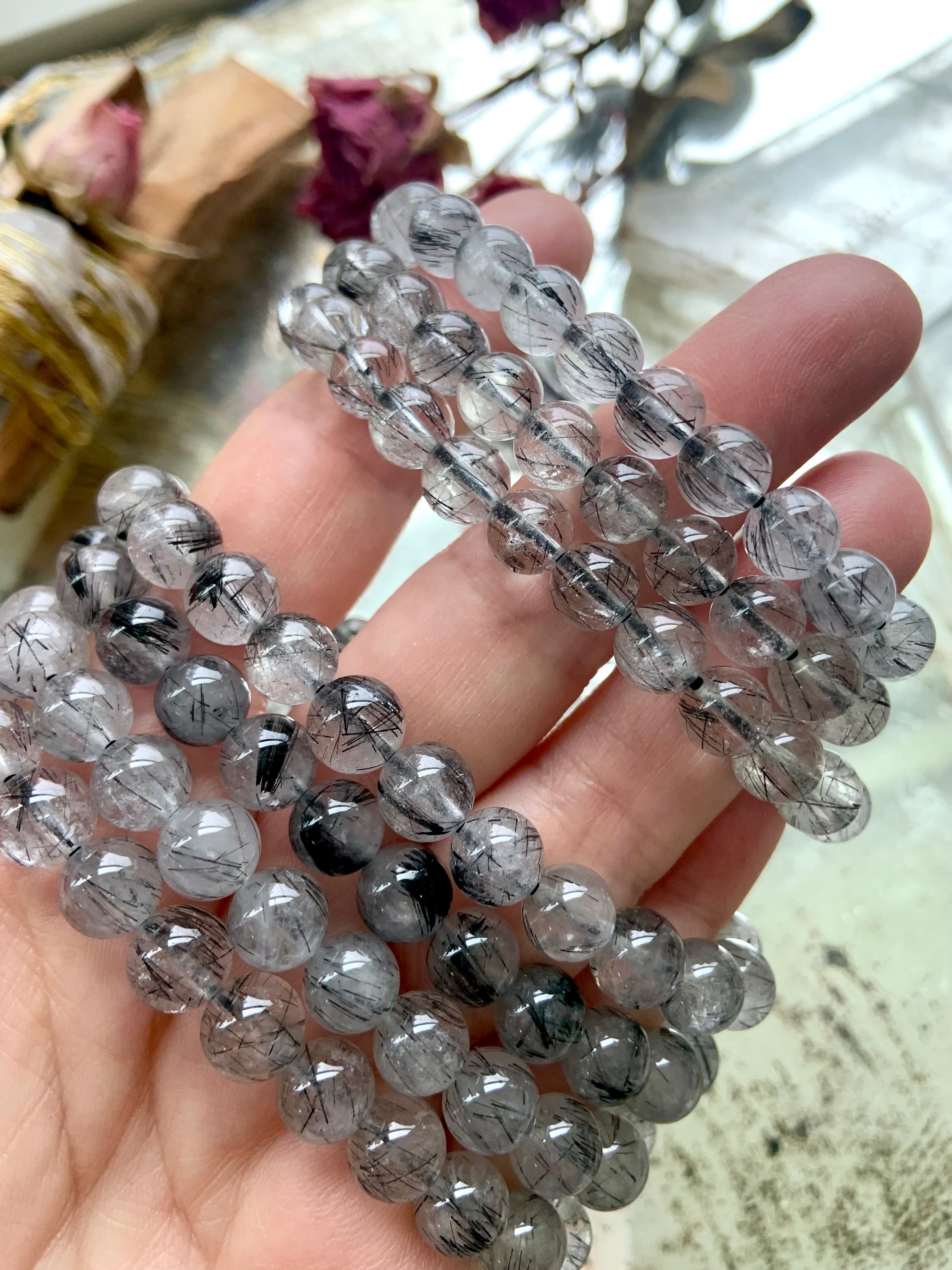 Closeup of a stack of Black Tourmaline in Quartz bracelets on a hand over a mirrored surface, showcasing the clarity and fine tourmaline inclusions